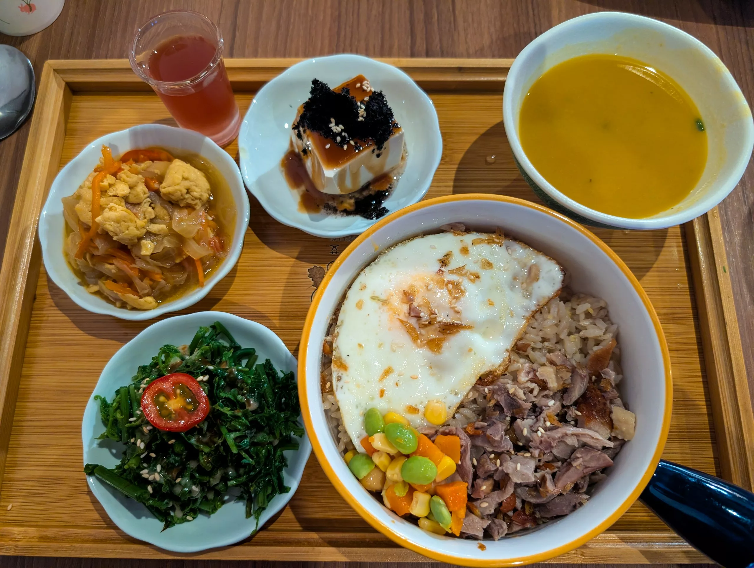 Un plateau avec un bol de riz garni d'un œuf au plat, de légumes mélangés et de viande accompagné de légumes verts cuits, de tofu avec une sauce aux algues, de légumes sautés et d'une soupe