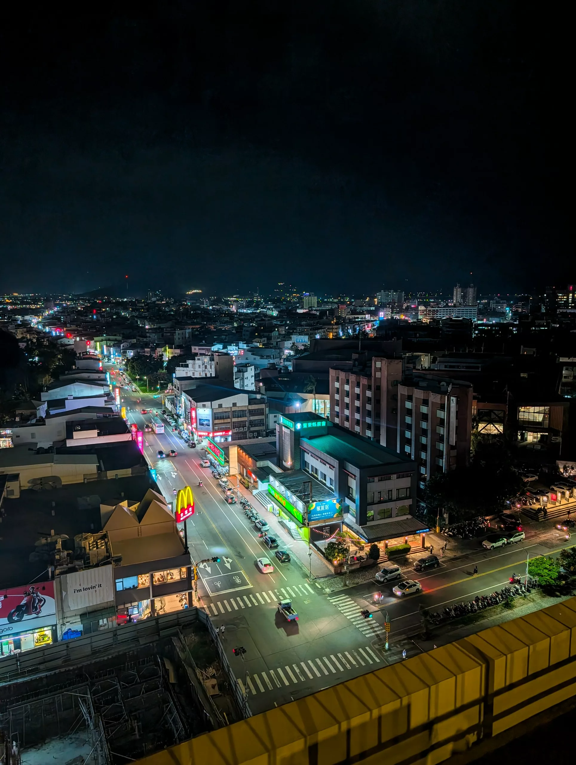 Un paysage urbain de nuit montre des rues brillamment éclairées, des voitures en mouvement, des bâtiments illuminés et une enseigne McDonald's.