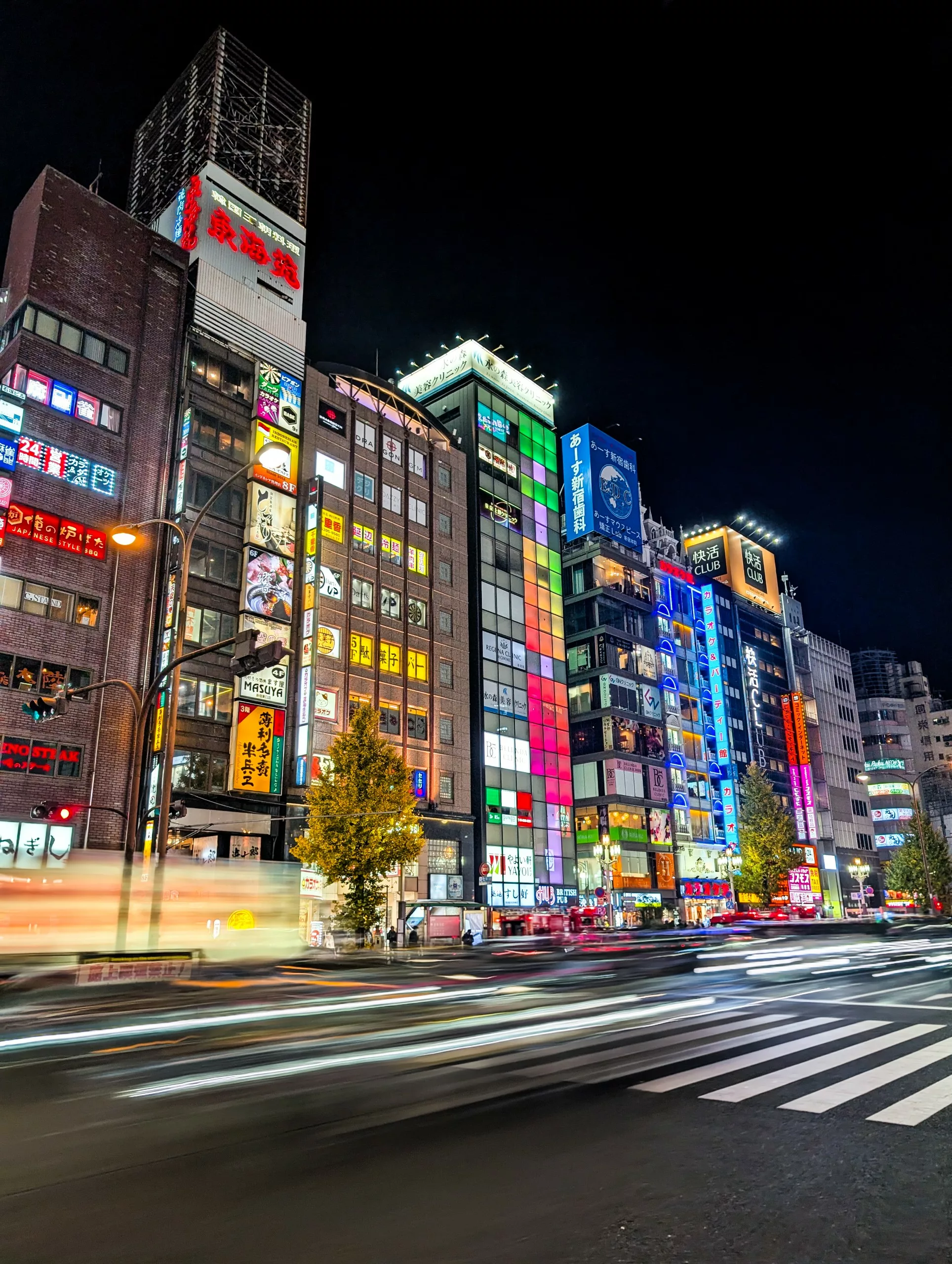 Une rue animée la nuit à Tokyo, avec de grands bâtiments ornés d'enseignes au néon et des traînées lumineuses des véhicules