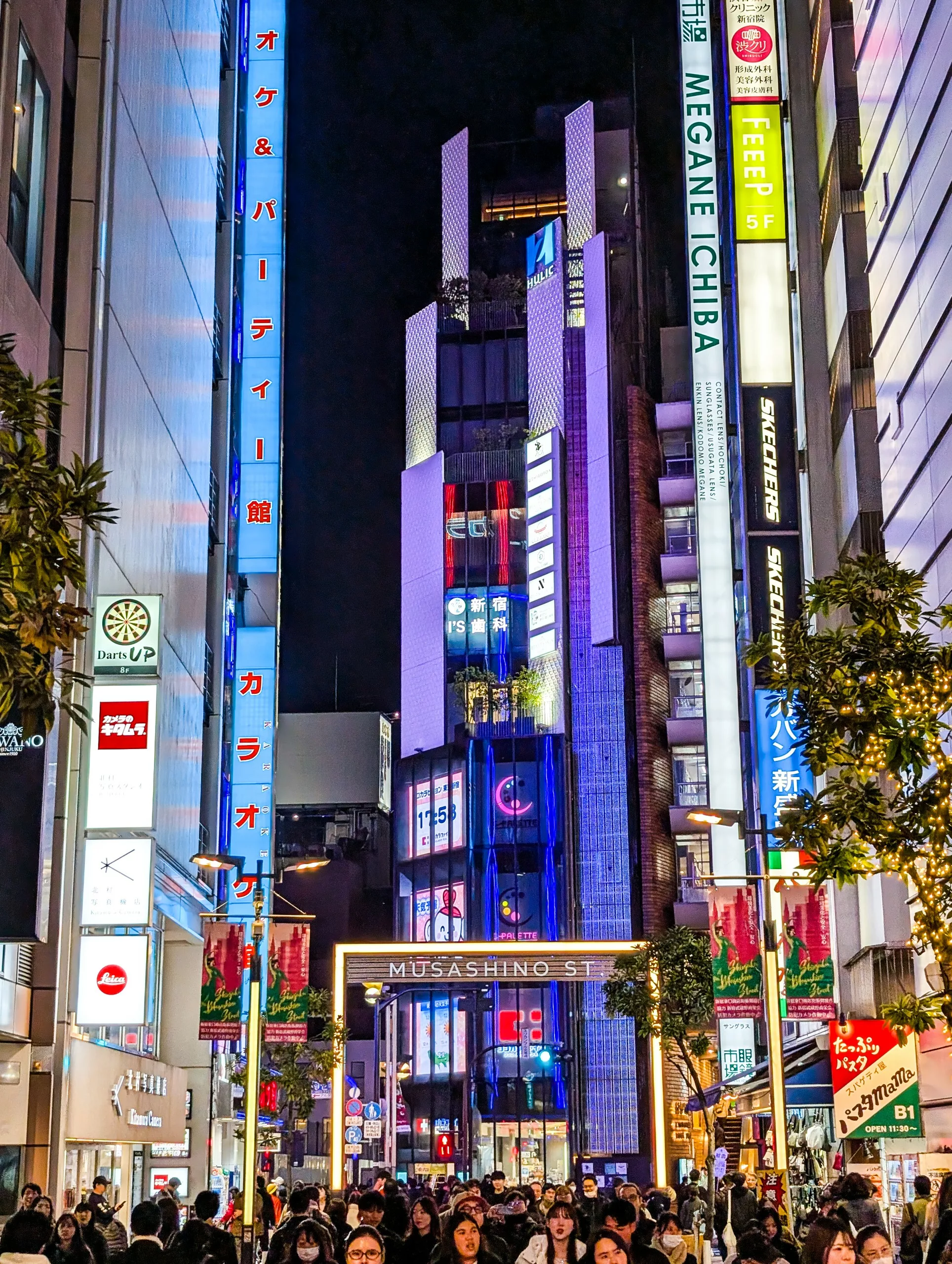 Une rue animée dans une zone urbaine la nuit, remplie de foules qui explorent ce qu'il faut faire à Tokyo- avec de grands bâtiments, des panneaux et des publicités colorées qui éclairent la scène.