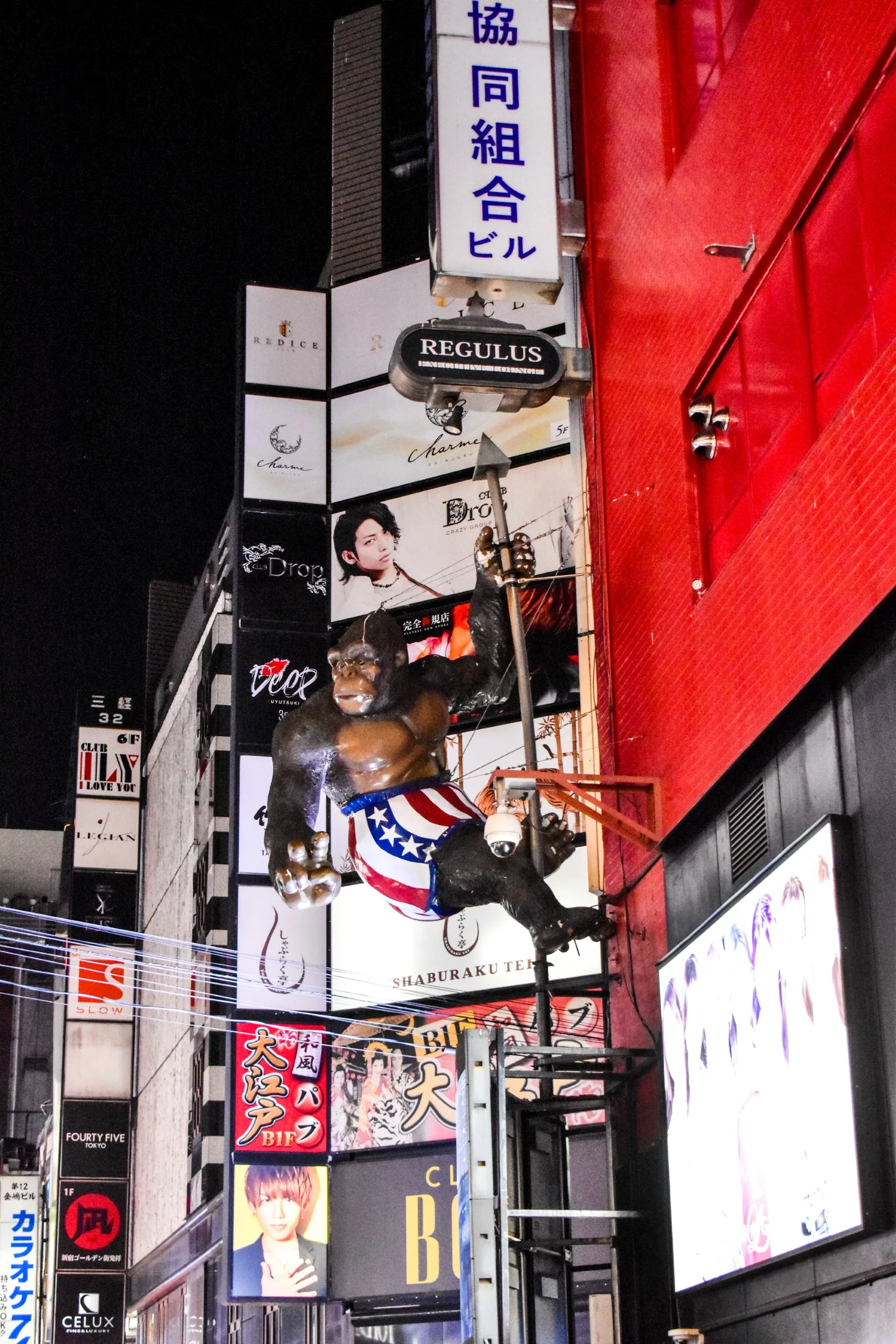 Une rue de Tokyo la nuit avec la grande statue du gorille King Kong en short américain accrochée à un bâtiment au milieu de panneaux publicitaires lumineux.