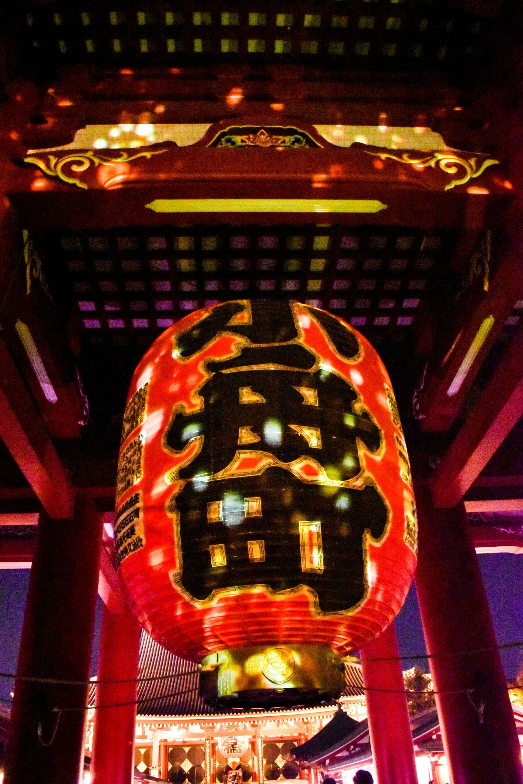 Grande lanterne en papier rouge avec des caractères japonais noirs et dorés accrochée sous la porte d'un temple la nuit, illuminée par des lumières colorées - une scène frappante pour tous ceux qui explorent ou cherchent quoi faire à Tokyo (que faire à Tokyo).