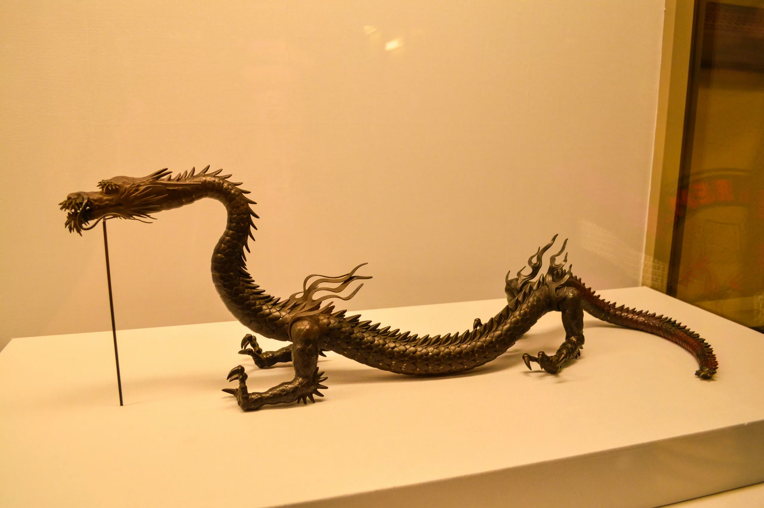 Une sculpture en bronze d'un dragon long et mince, doté de quatre pattes, d'un dos hérissé et d'une gueule ouverte, est exposée sur une plate-forme blanche. Il s'agit d'une visite incontournable si vous souhaitez découvrir que faire à Tokyo dans le cadre d'un musée.