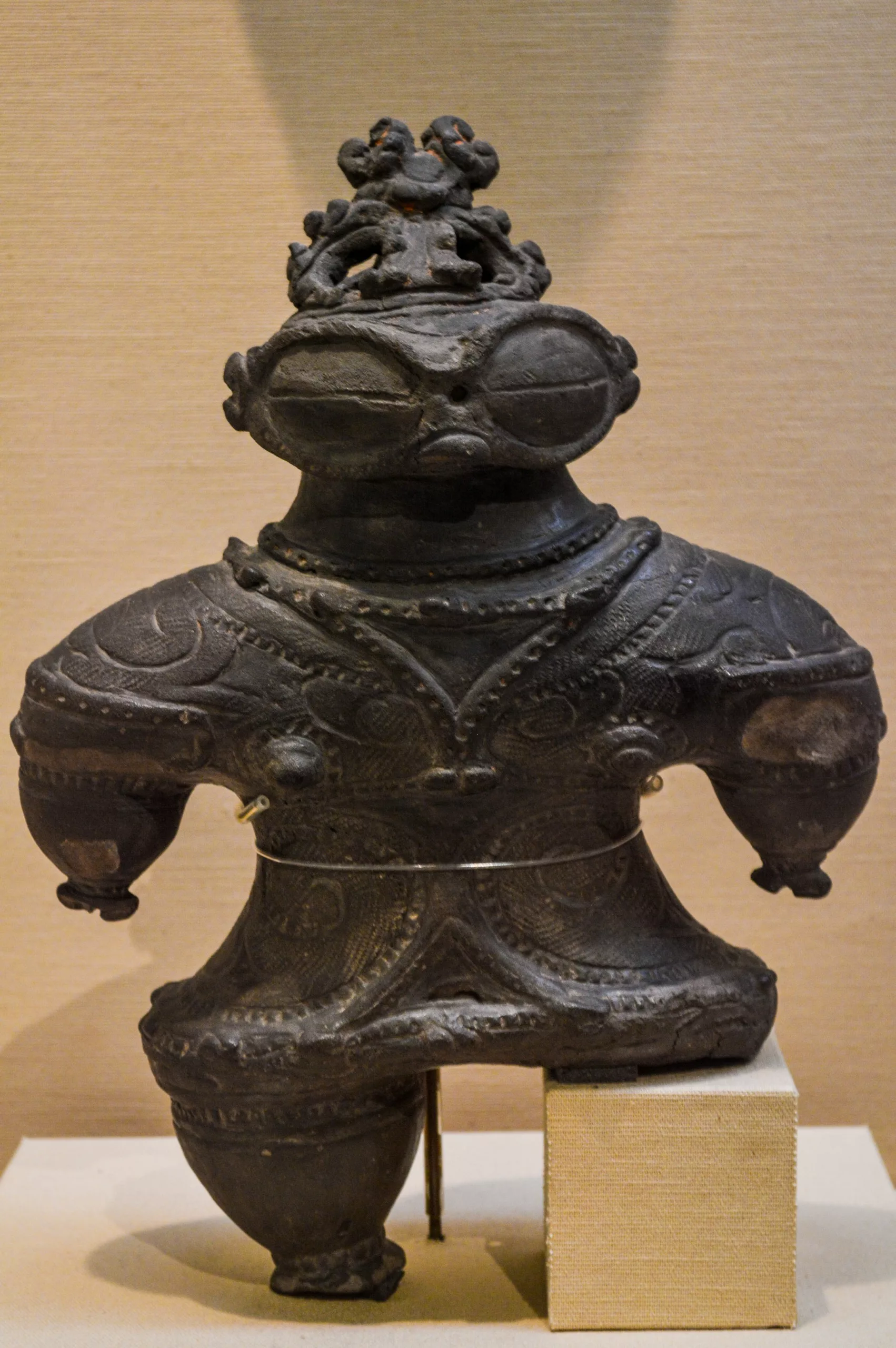 Figurine humanoïde en argile, sombre et décorée de façon complexe, avec de grands yeux ronds et une coiffe détaillée - un artefact que vous pourriez découvrir en explorant les musées lors de votre aventure "que faire à Tokyo".