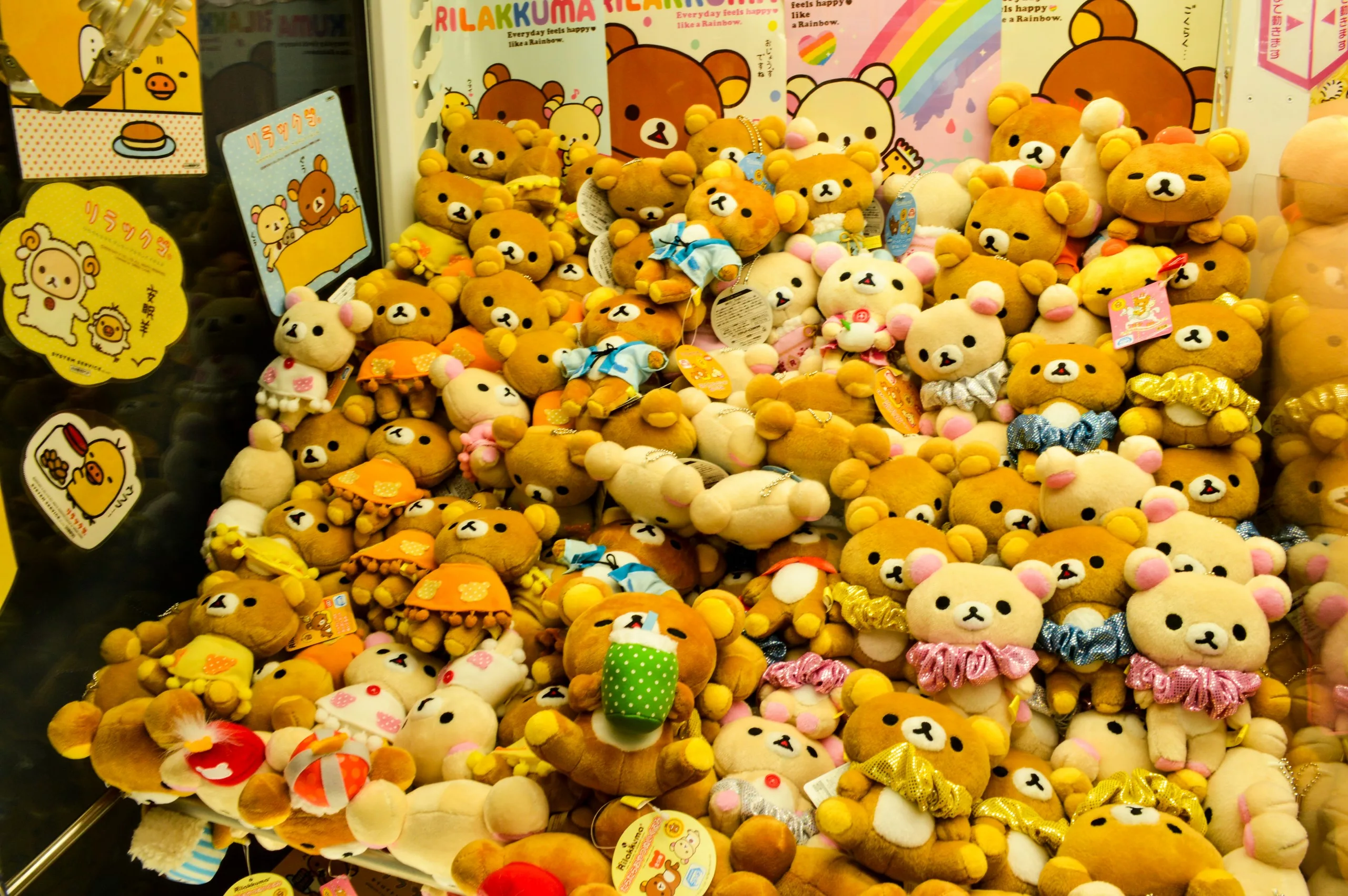 Une grande pile de peluches Rilakkuma, certaines vêtues de tenues colorées, exposées à l'intérieur d'une machine à griffes