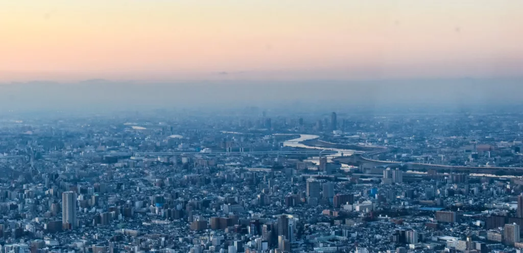 Une large vue aérienne de Tokyo au coucher du soleil, avec des bâtiments densément peuplés, une rivière sinueuse et un ciel pastel - pour capturer le paysage urbain vibrant et inspirer votre liste de ce qu'il faut faire à Tokyo.