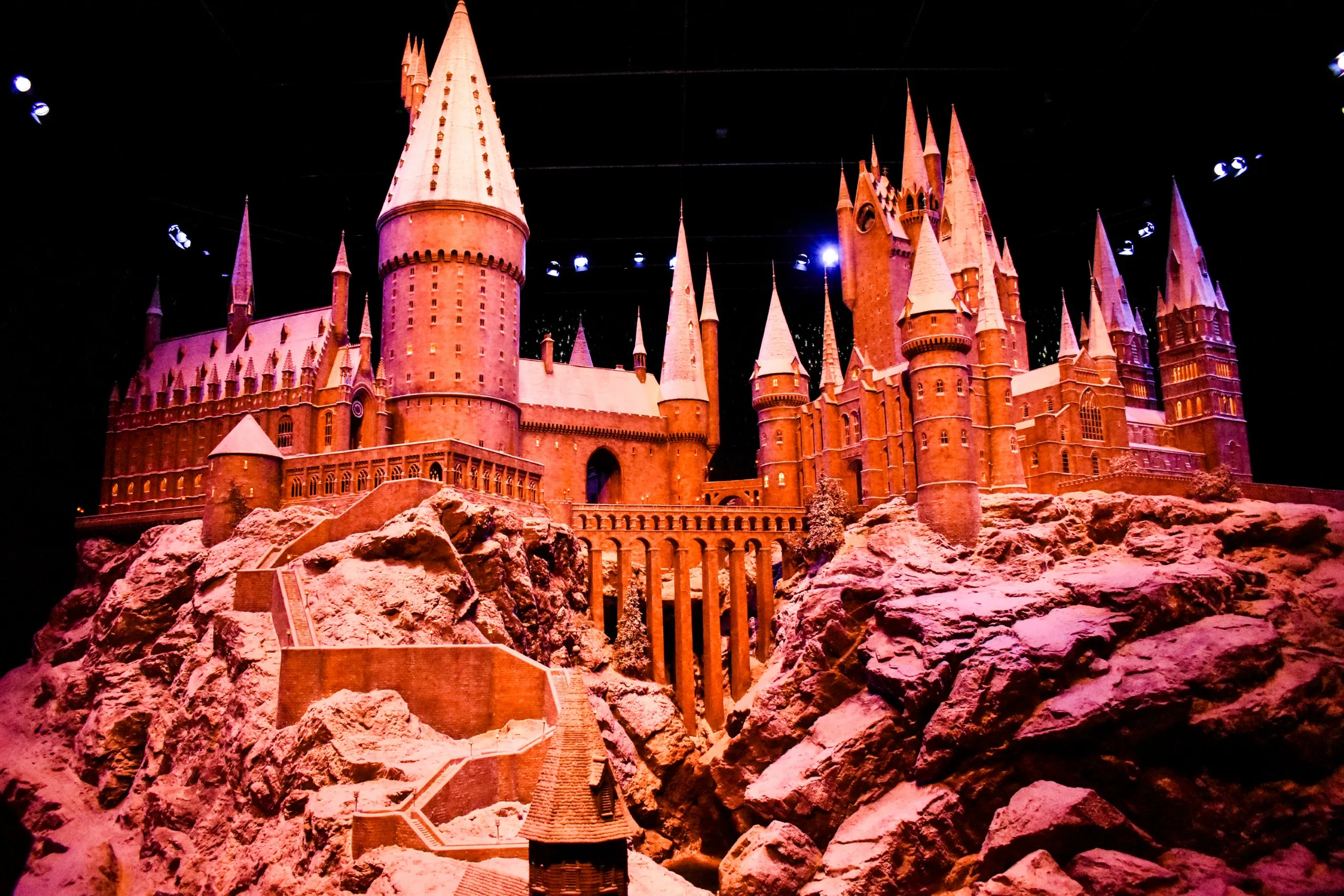 Un modèle détaillé d'un grand château de style fantastique avec de multiples tours et flèches, situé sur une base rocheuse - comme ce que l'on peut voir en explorant Que faire à Tokyo- éclairé par un éclairage dramatique sur un fond sombre.