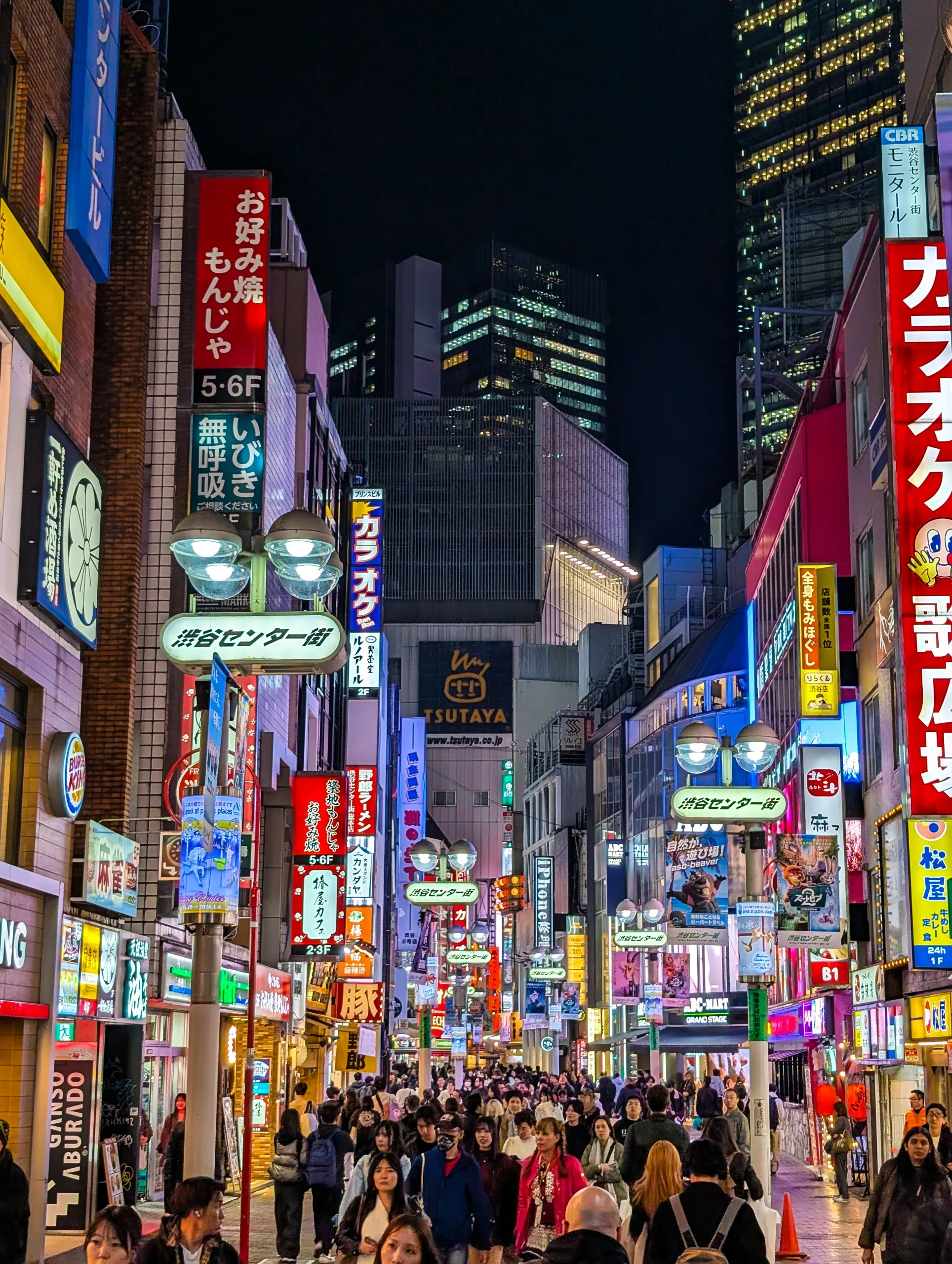 Une rue animée la nuit à Tokyo, remplie de gens qui marchent sous des bâtiments brillamment éclairés et des enseignes japonaises colorées