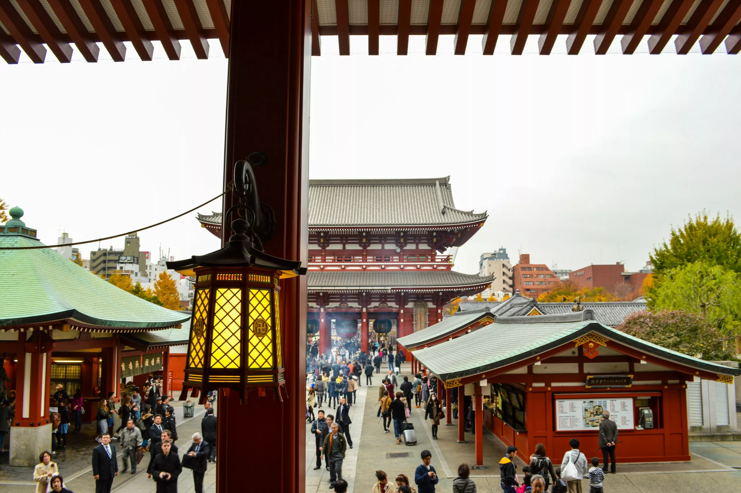 Vue d'une cour de temple animée avec des gens qui marchent, des bâtiments traditionnels rouges et une lanterne suspendue