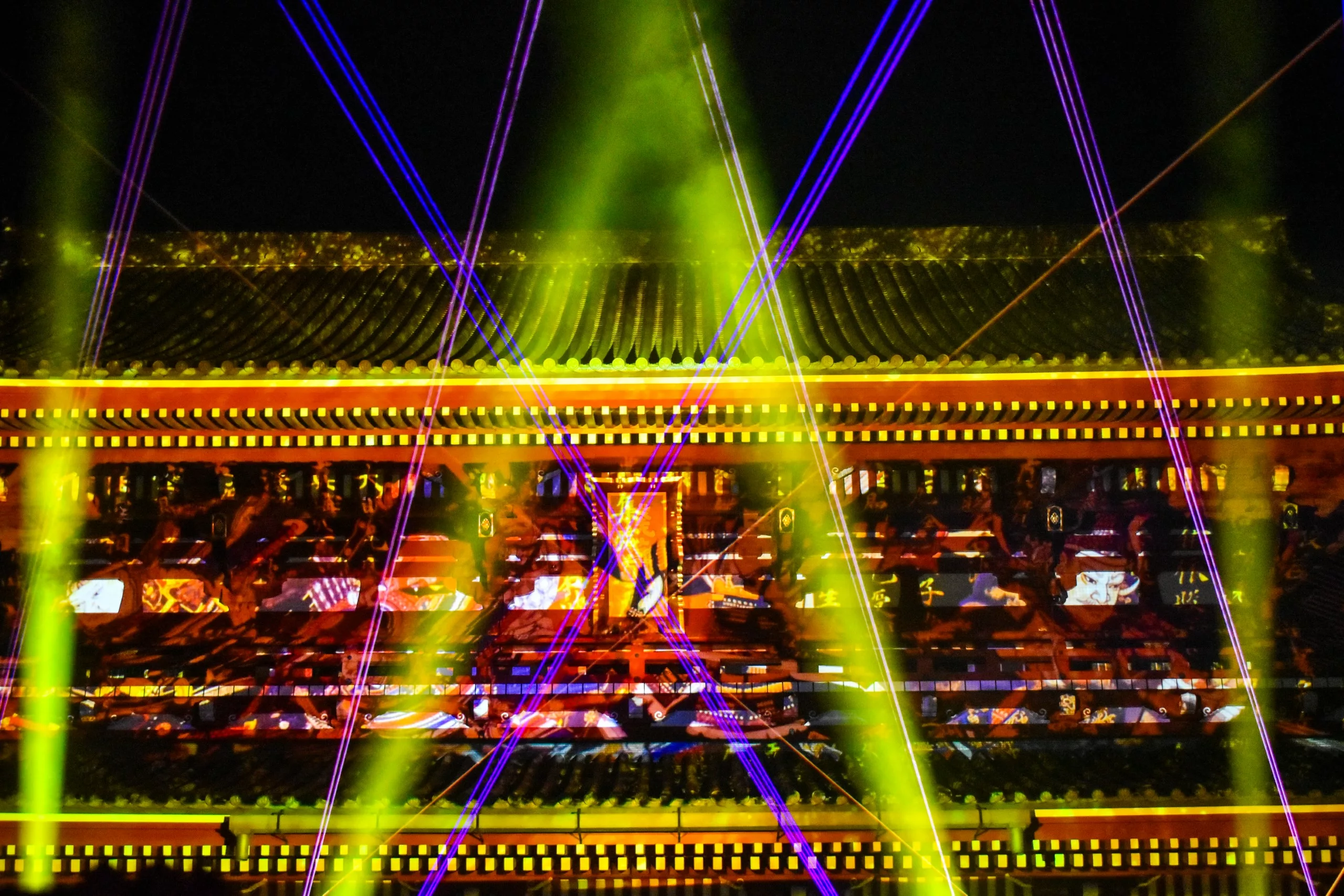 Un bâtiment asiatique traditionnel est illuminé la nuit par des faisceaux jaunes brillants et des motifs colorés projetés - un spectacle visuel vibrant à ne pas manquer pour tous ceux qui se demandent ce qu'il faut faire à Tokyo.