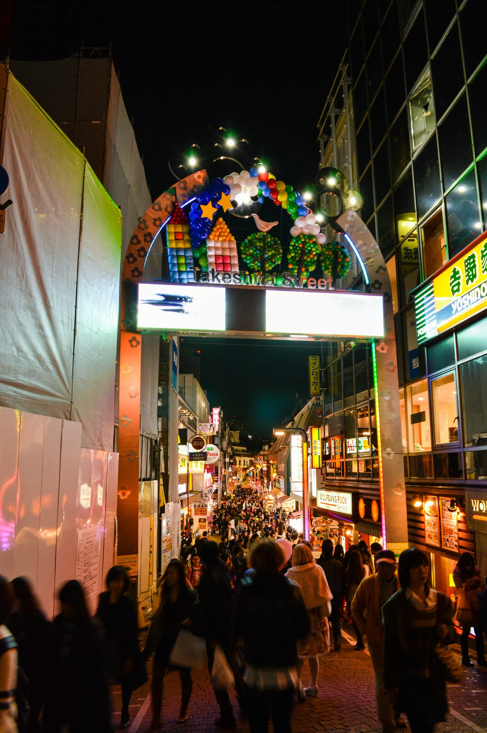 Une rue commerçante animée la nuit, avec des lumières vives, des enseignes colorées et une arche décorative - l'une des meilleures suggestions pour que faire à Tokyo. De nombreuses personnes flânent devant les boutiques qui bordent les deux côtés de cette rue animée.