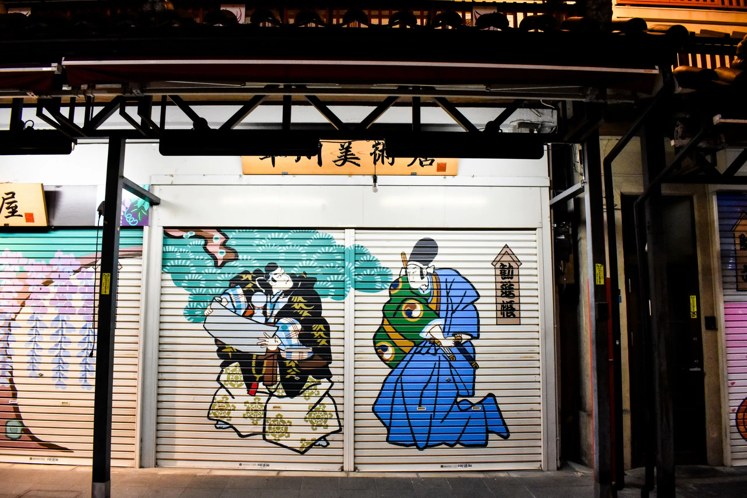 Une devanture de magasin dont le volet métallique est peint dans un style japonais traditionnel, représentant deux personnages en robes colorées et des nuages stylisés - un spectacle unique si vous explorez la ville et vous demandez que faire à Tokyo.