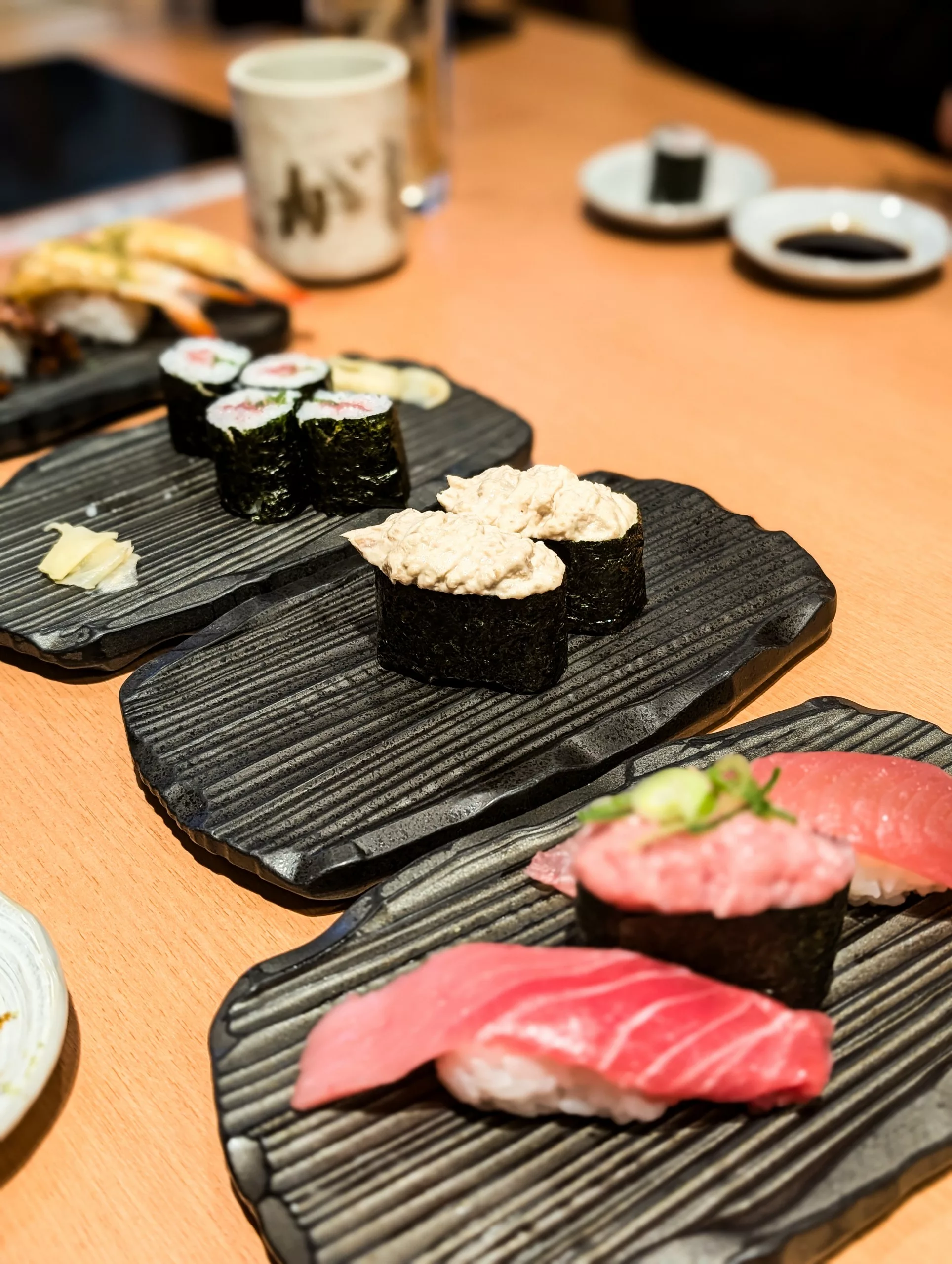 Des assiettes de sushis assortis, dont des nigiri au thon, des gunkan-maki à la garniture crémeuse et des rouleaux maki, sont disposées sur une table 