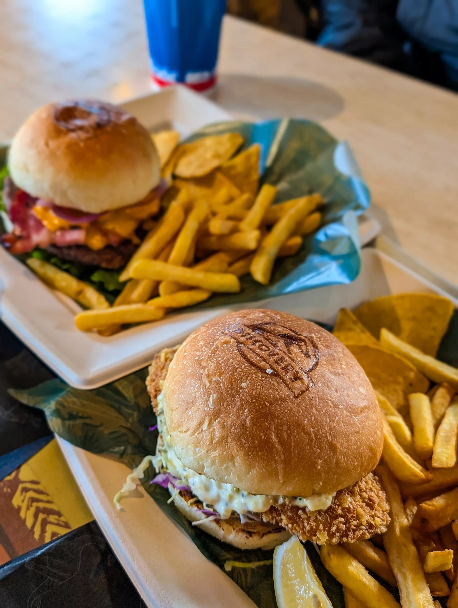 Deux assiettes sur une table à Osaka : l'une contient un sandwich au poulet frit et du coleslaw, l'autre un cheeseburger avec de la laitue et des tomates. 