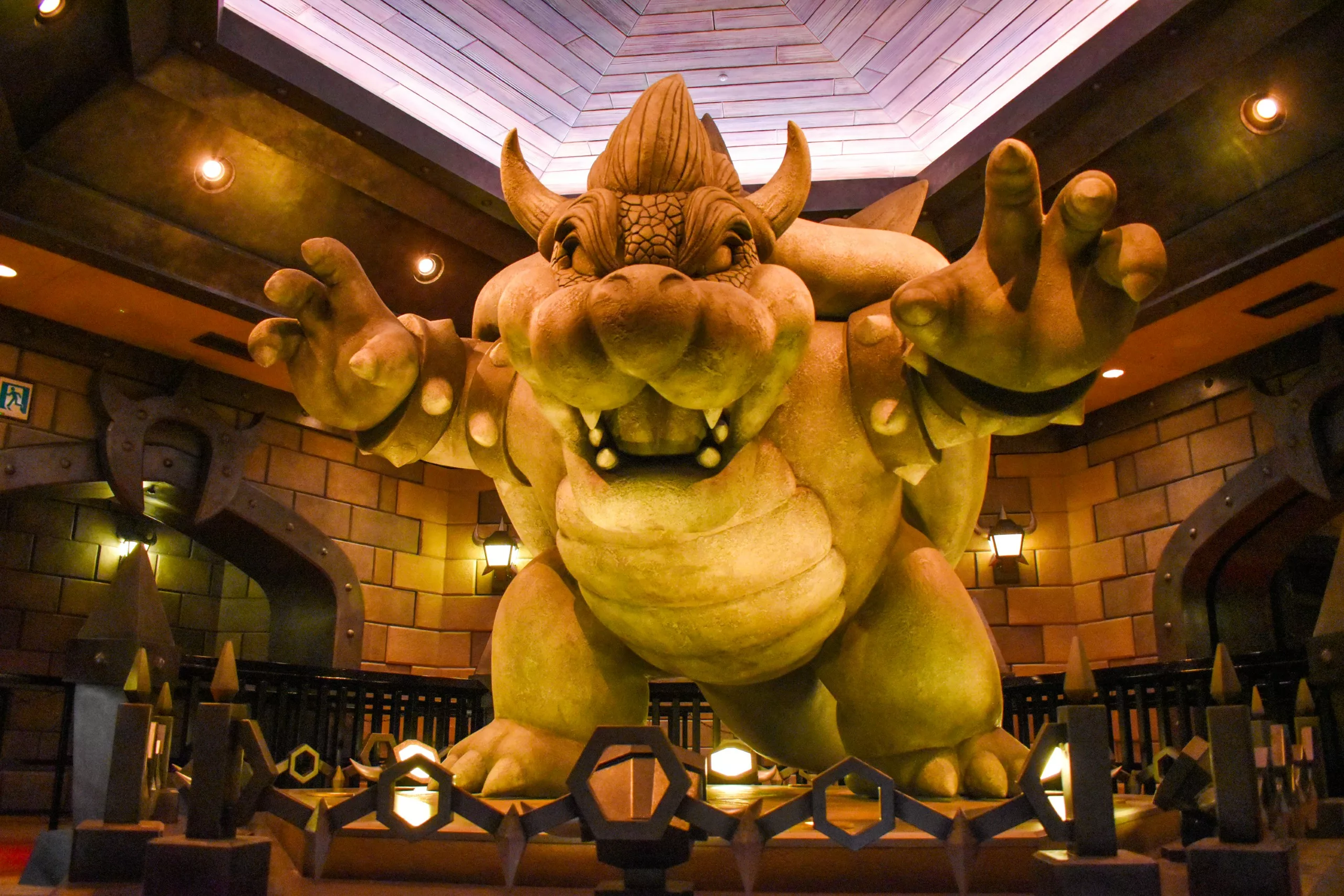 Une grande statue de Bowser, un personnage en forme de tortue de la série de jeux vidéo Mario, se dresse, les bras tendus, dans un décor faiblement éclairé