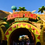 L'entrée de Donkey Kong Country à Universal Studios Japan à Osaka présente un grand panneau jaune et rouge avec des palmiers et des murs en pierre, sous lesquels les gens passent
