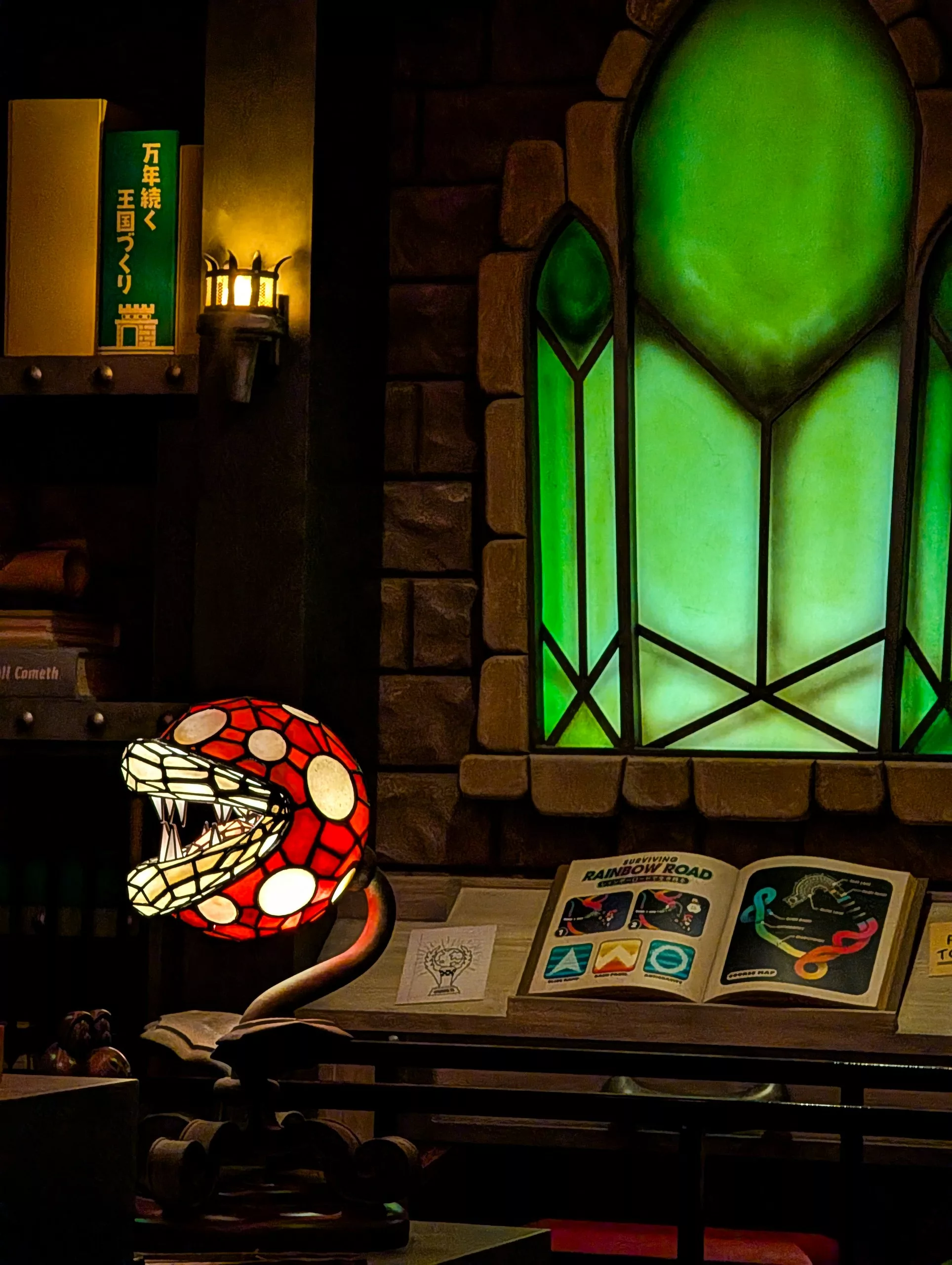 Une salle d'étude avec un vitrail vert, des livres ouverts sur un bureau et une lampe en forme de tête de serpent rouge et blanc aux dents acérées