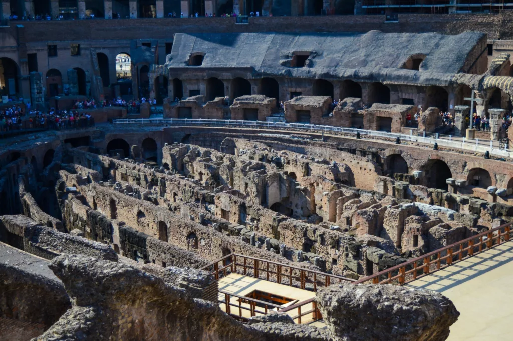 Vue intérieure du Colisée romain à Rome, avec ses murs en pierre, ses arches et ses structures souterraines exposées.