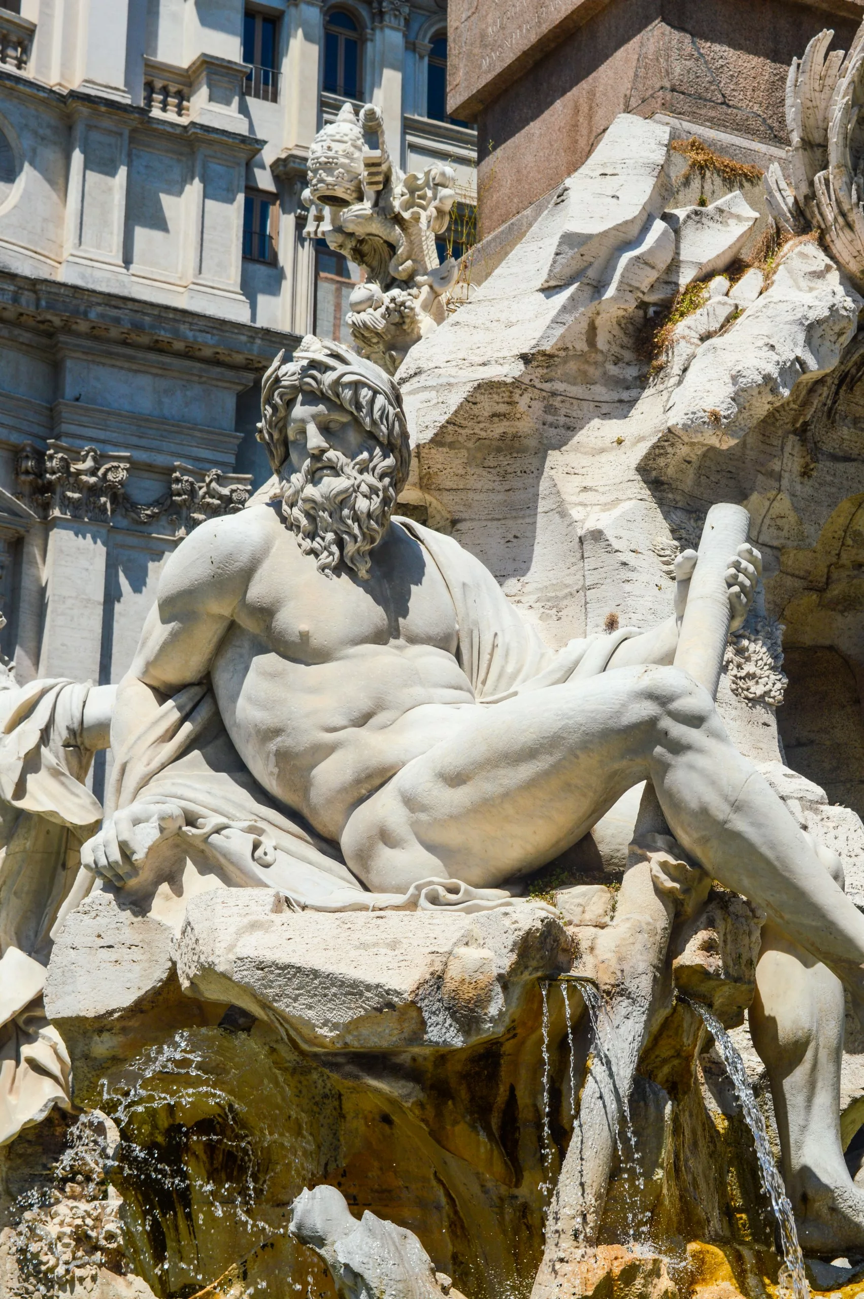 Vue rapprochée d'une statue masculine allongée avec une barbe, partiellement drapée dans un tissu, faisant partie d'une fontaine en pierre 