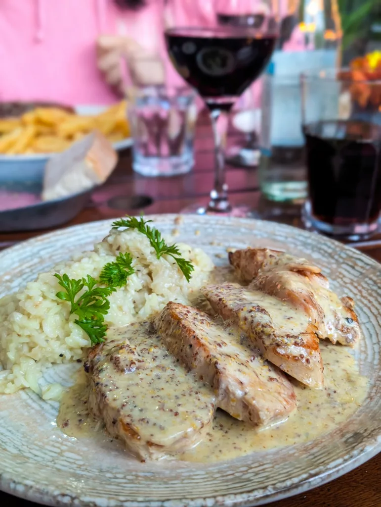 Une assiette avec des tranches de blanc de poulet dans une sauce crémeuse à la moutarde, servie avec du riz garni de persil. Un verre de vin rouge est posé à côté.