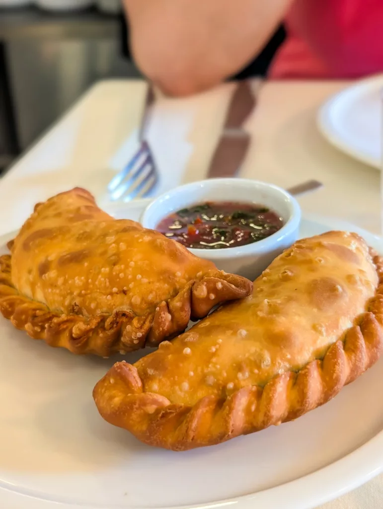 Deux empanadas frites et dorées sont servies sur une assiette blanche avec une sauce pour les tremper.