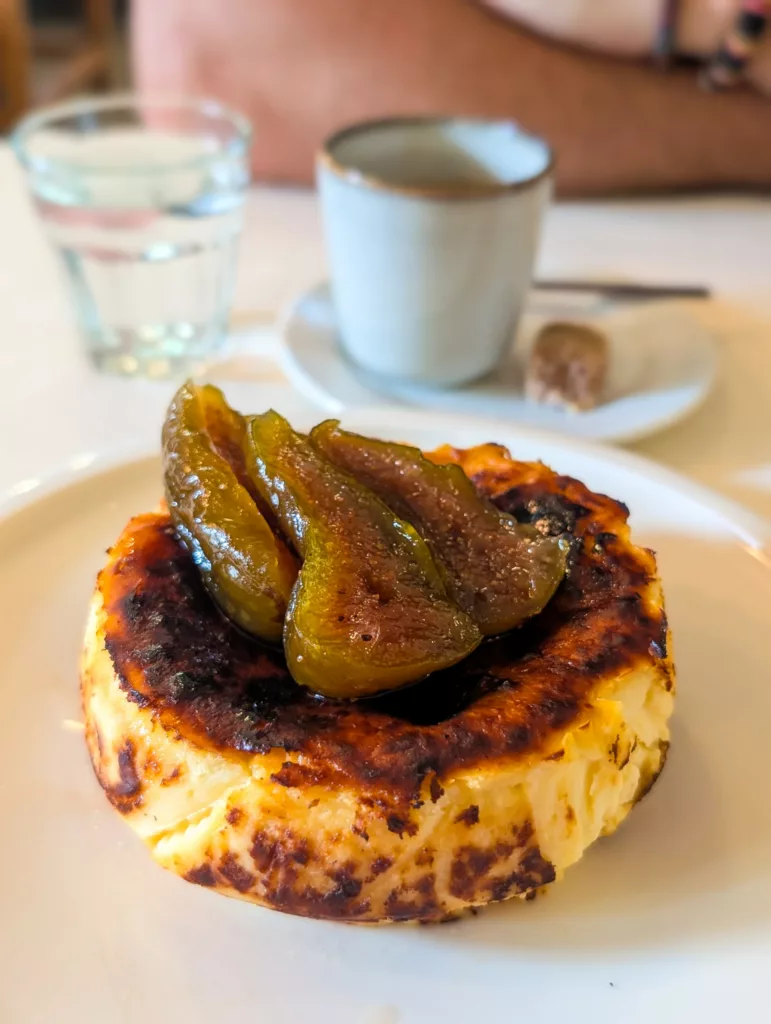 Tarte basque au fromage ronde avec des figues dessus. Un café à l'arrière-plan.
