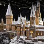 Une maquette détaillée d'un grand château de style médiéval avec de nombreuses tours et tourelles pointues, recouverte de neige, exposée à l'intérieur sous les projecteurs du Studio Harry Potter Tokyo.