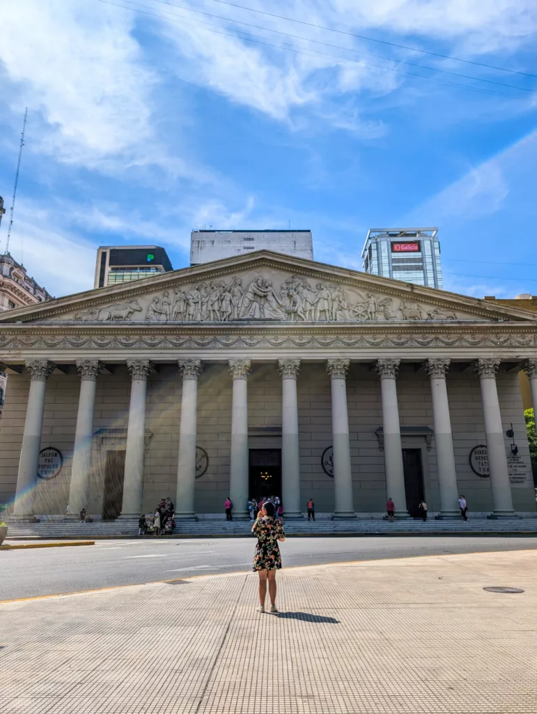 Une femme vêtue d'une robe à fleurs se tient face à un bâtiment néoclassique à grandes colonnes à Buenos Aires.