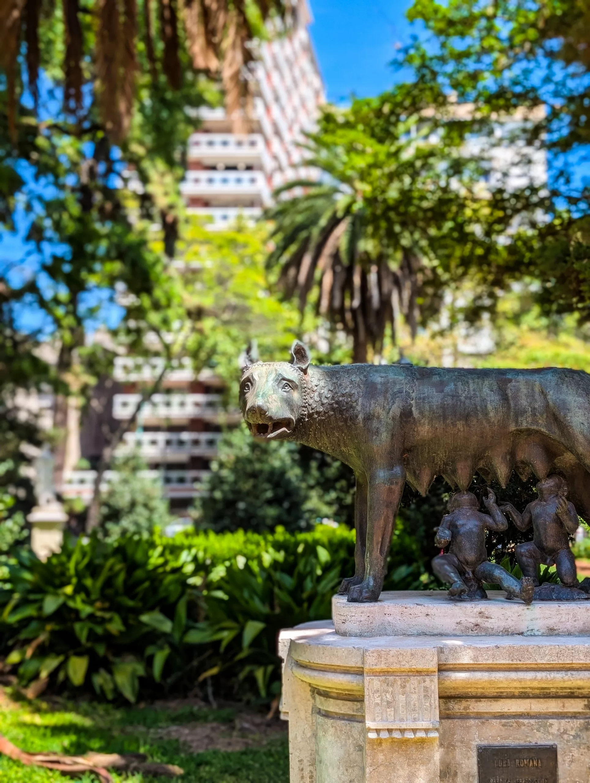 Dans un parc de Buenos Aires, entourée de verdure et surplombée par un grand immeuble d'habitation, la statue en bronze d'une louve et de deux silhouettes humaines se dresse sur un piédestal.
