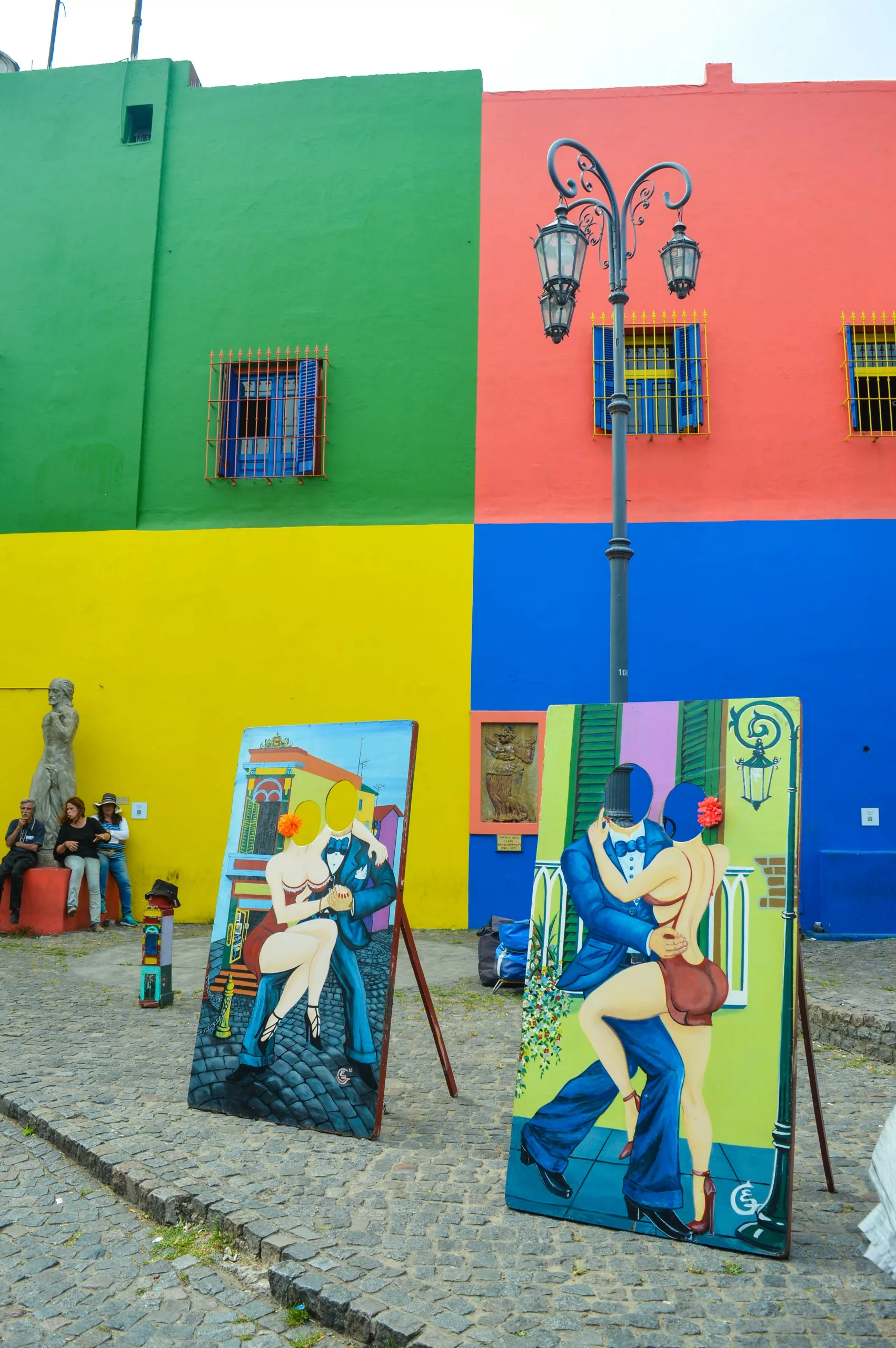 Deux peintures colorées de danseurs de tango sur des chevalets égayent une rue pavée devant un bâtiment dynamique