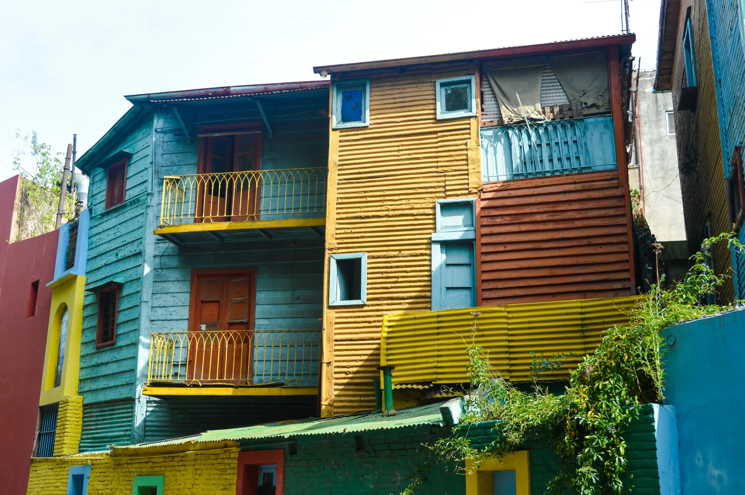 Trois maisons reliées entre elles par un bardage en bois peint en bleu, jaune et rouge - chacune avec des balcons et des portes colorée.