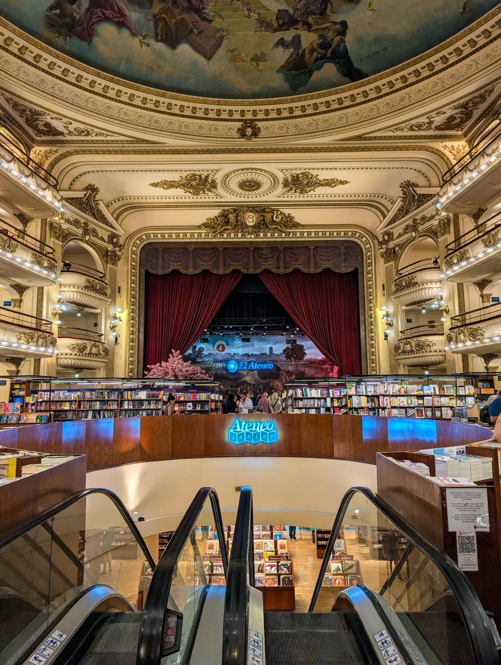 Intérieur d'une librairie à Buenos Aires, avec de hauts plafonds, une coupole peinte et des balcons de style théâtre garnis de livres. Un escalator descend à un niveau inférieur.