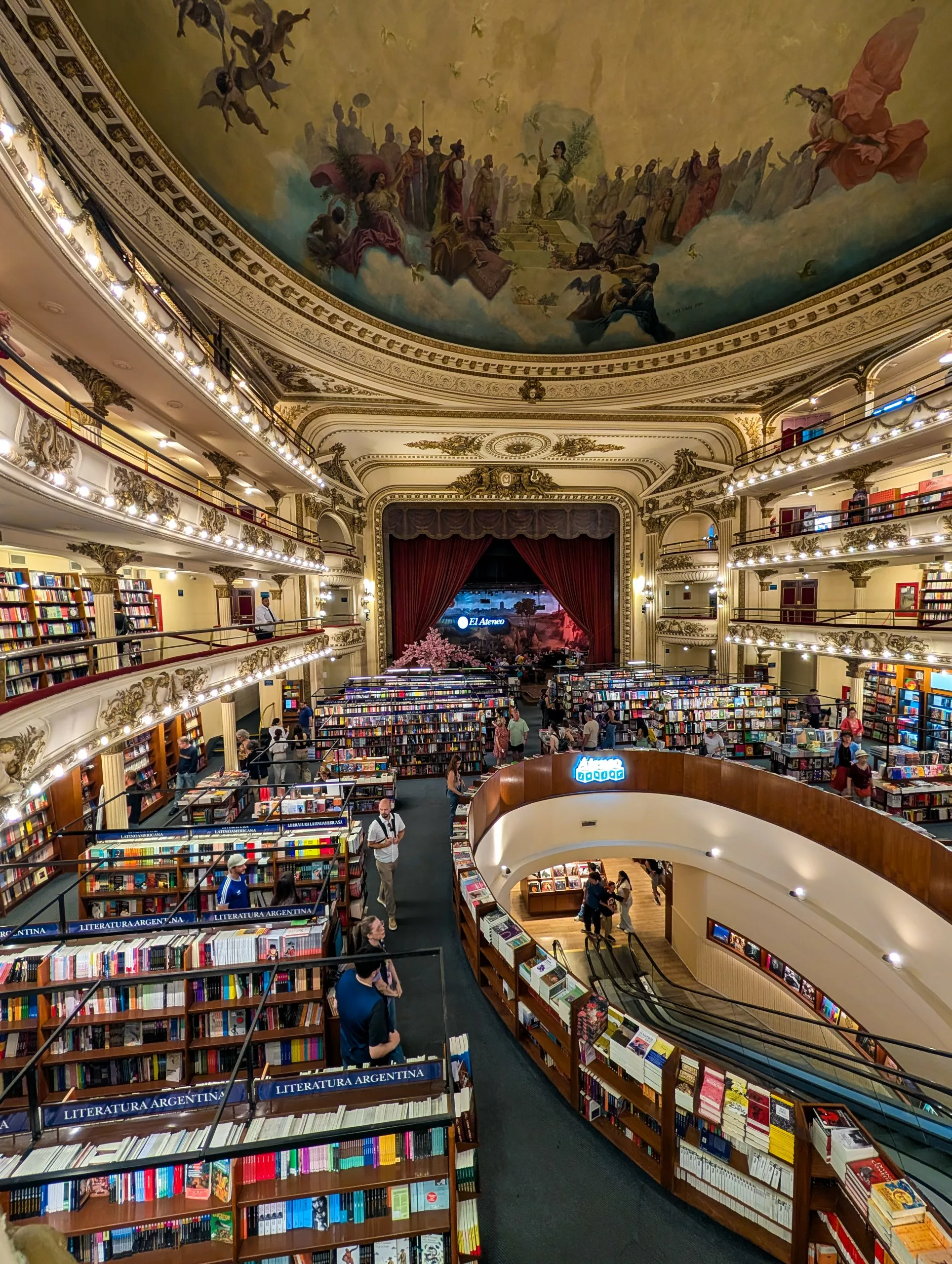Une librairie spacieuse avec plusieurs niveaux d'étagères, un plafond en dôme avec une peinture murale et un rideau de scène en velours rouge