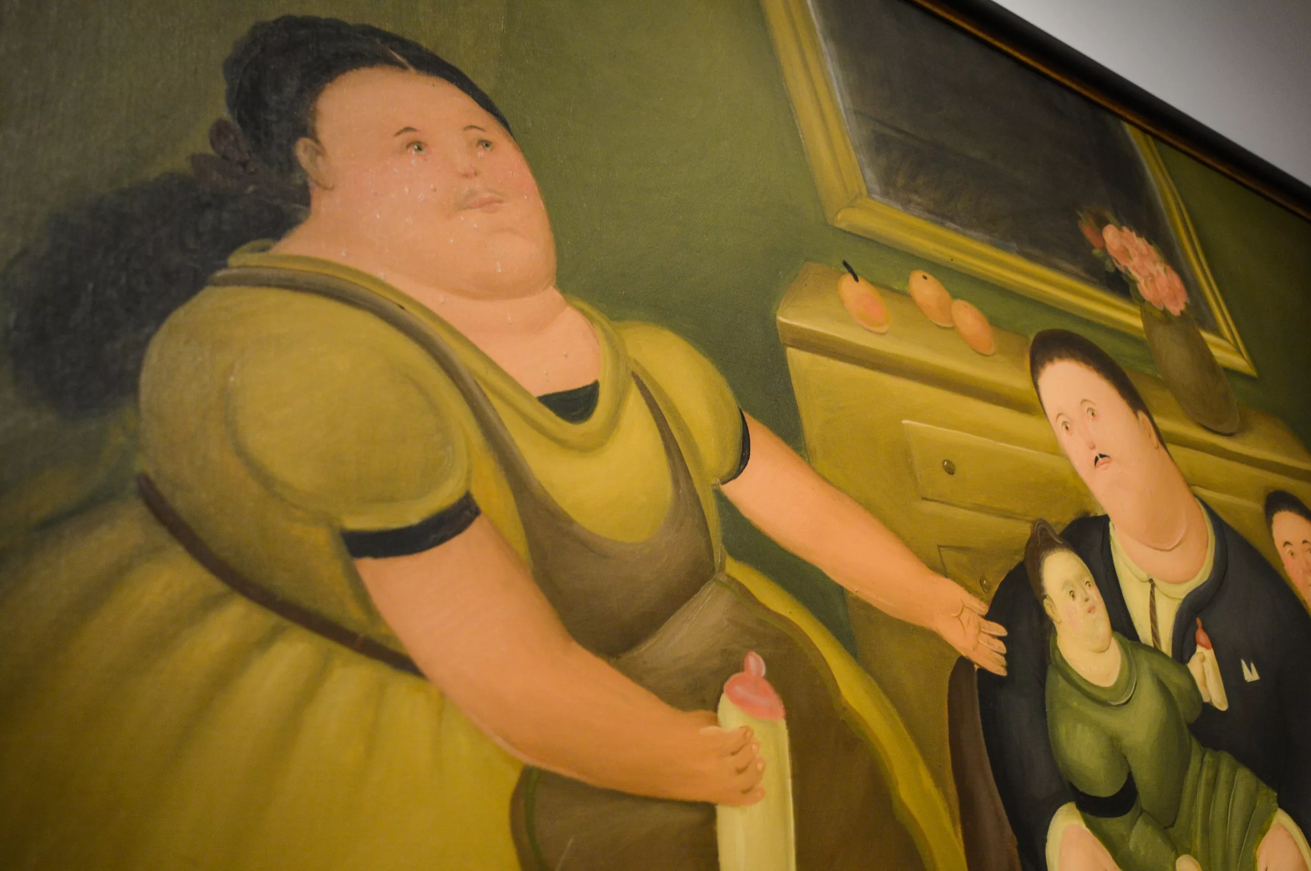 Un tableau représente plusieurs personnages aux traits exagérés et arrondis. Au premier plan, une femme vêtue d'une robe jaune tient un biberon. Une commode avec des fruits et un miroir apparaît à l'arrière-plan.