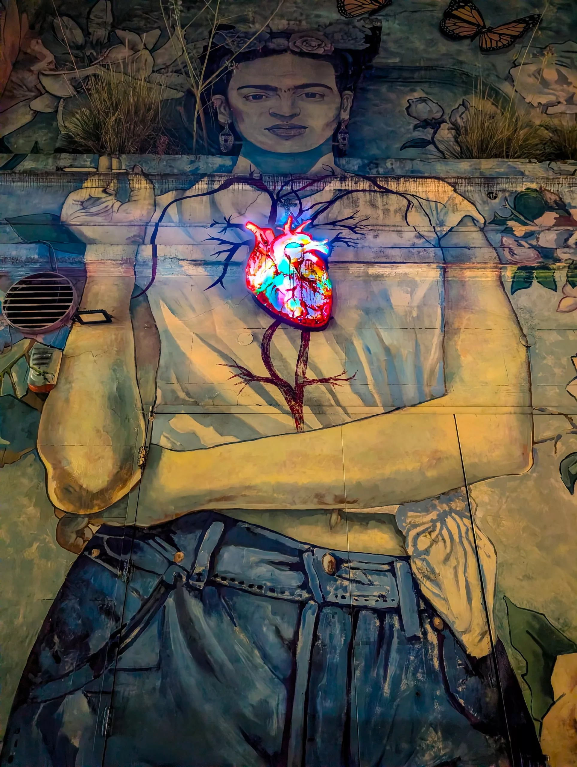 Une peinture murale du quartier Palermo, représentant Frida Kahlo avec des vêtements modernes et un cœur illuminé avec des artères visibles et des papillons au-dessus