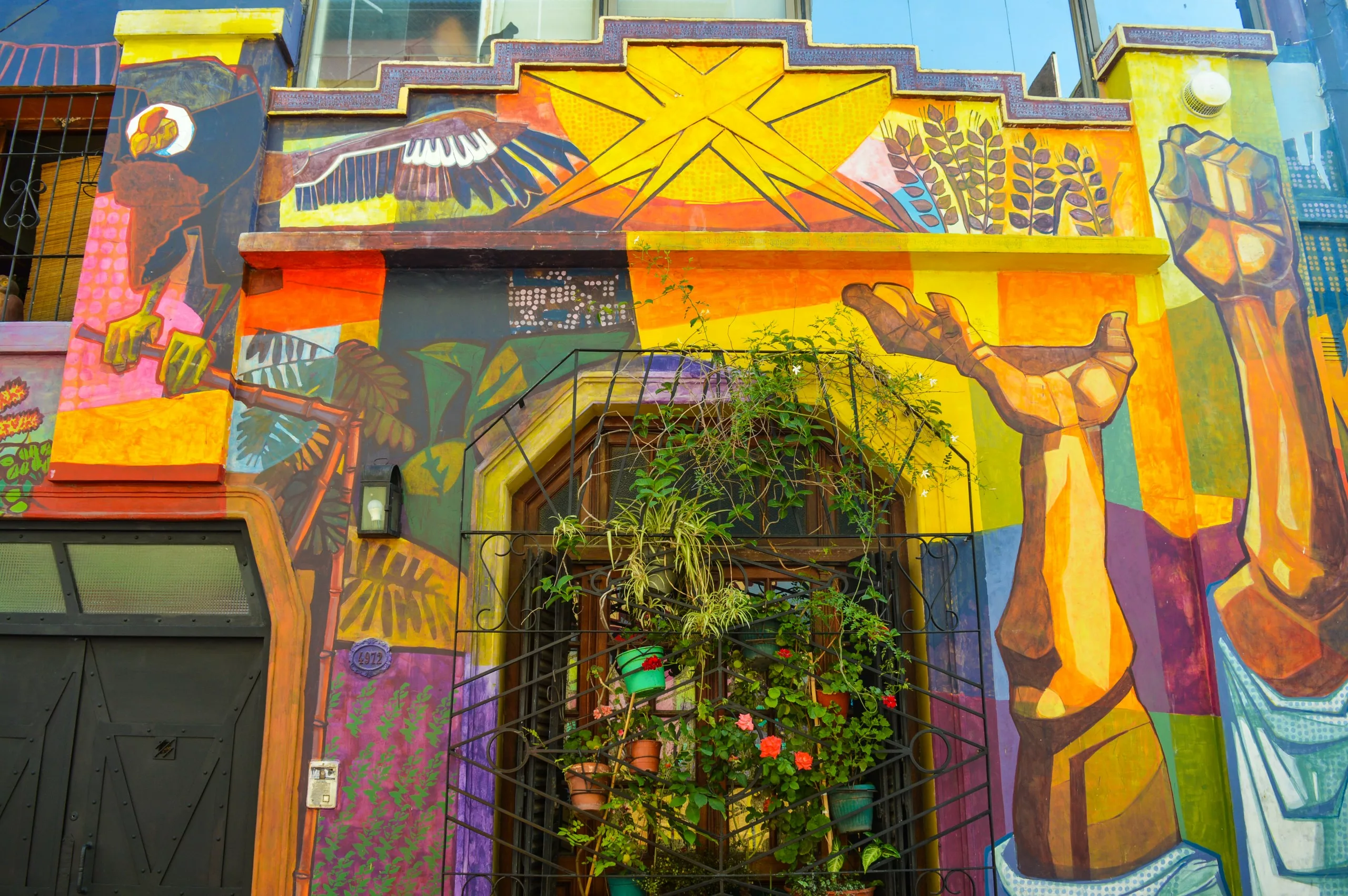Une façade de bâtiment peinte d'une peinture murale colorée représentant des formes géométriques, une main tendue, des plantes et un oiseau.