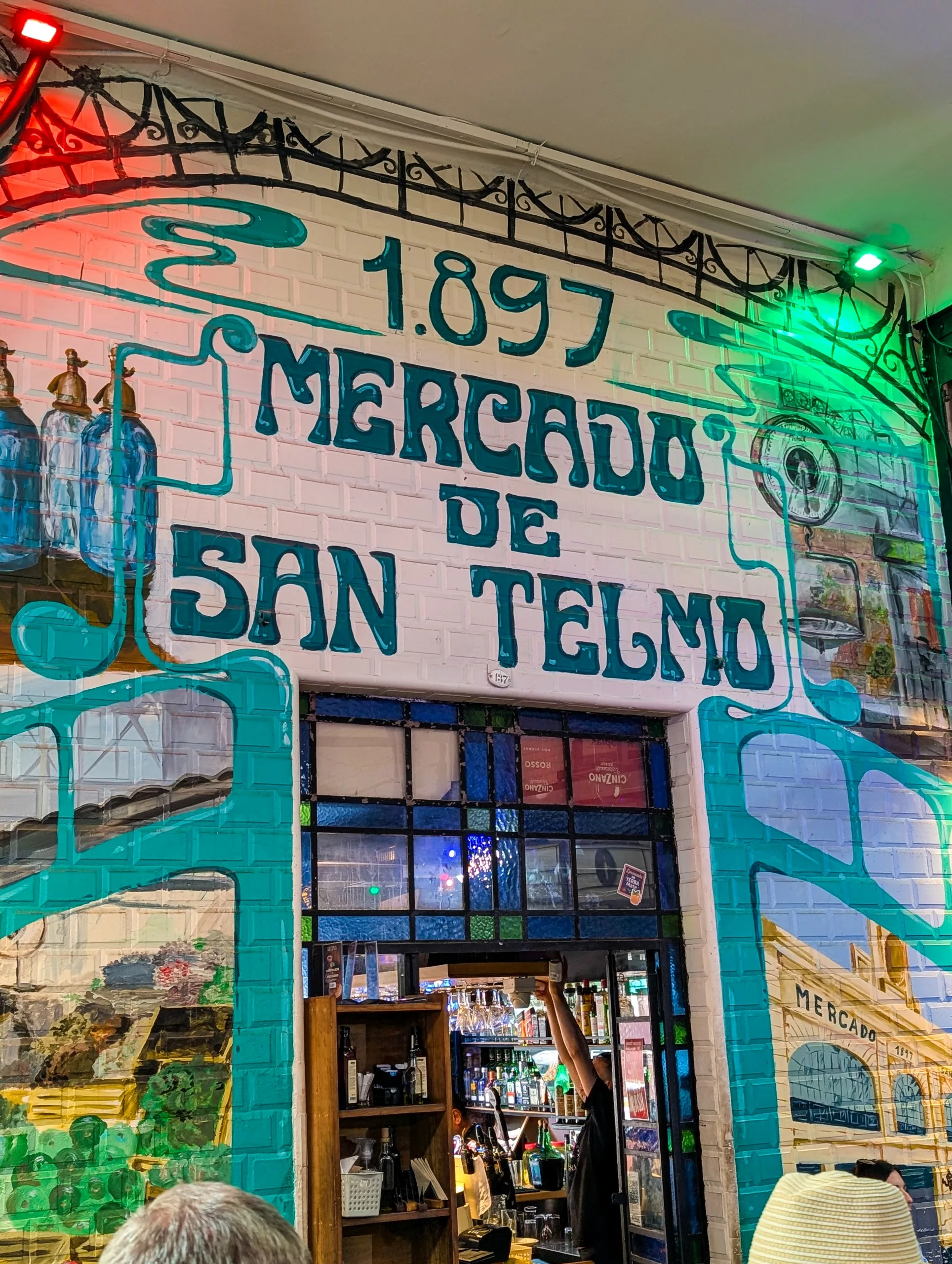 Une peinture murale sur un mur de briques affiche "1897 Mercado de San Telmo" au-dessus d'une porte en vitrail. Il y a aussi des illustrations sur le thème du marché
