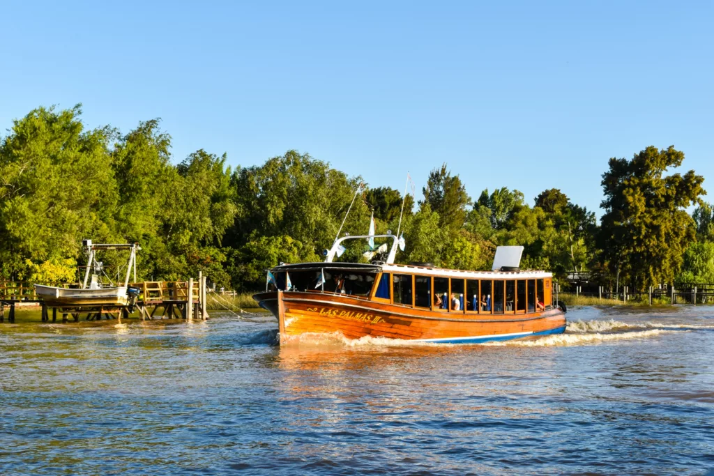 Un bateau de passagers en bois navigue sur une rivière avec des arbres et un petit quai en arrière-plan