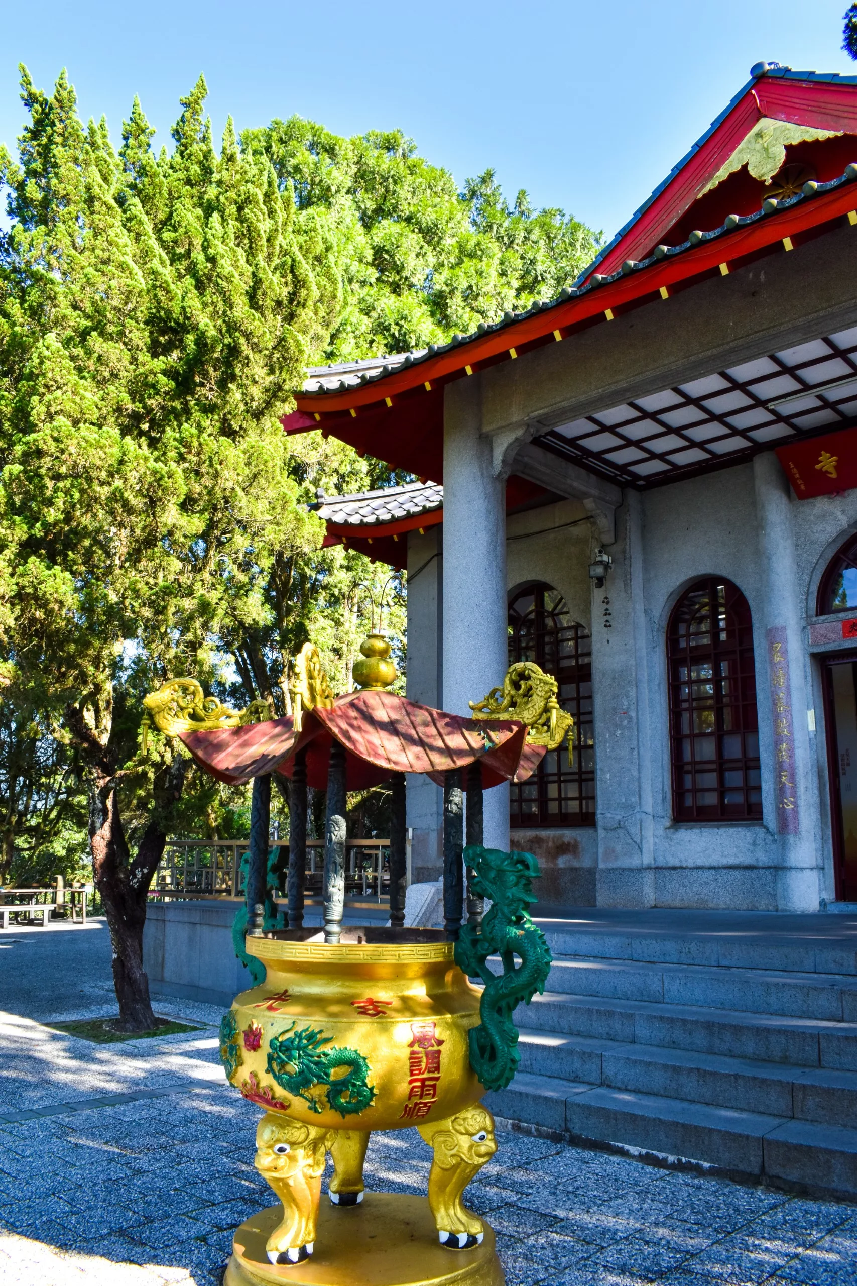 Un brûleur d'encens jaune décoré de dragons se dresse devant un bâtiment traditionnel de style chinois avec des tuiles rouges