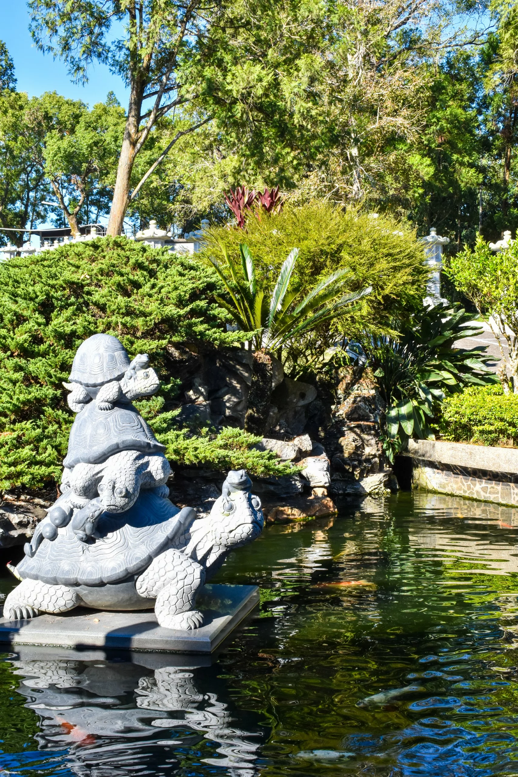 Une statue de pierre représentant deux tortues, l'une empilée sur l'autre, se dresse sur une plate-forme, entouré d'une végétation luxuriante et d'arbres