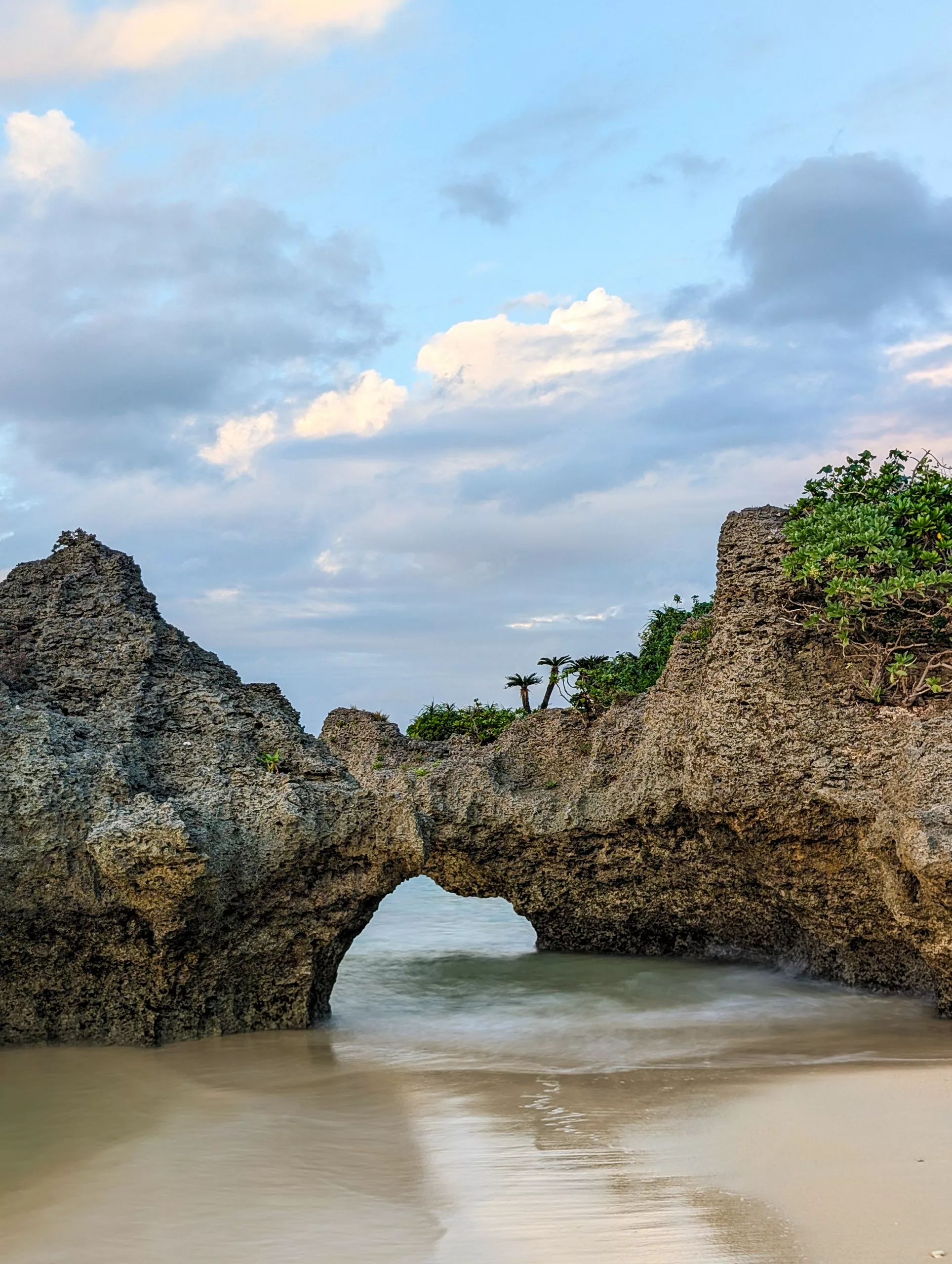 Une formation rocheuse dentelée formant une arche naturelle au-dessus d'une eau peu profonde sur une plage de sable