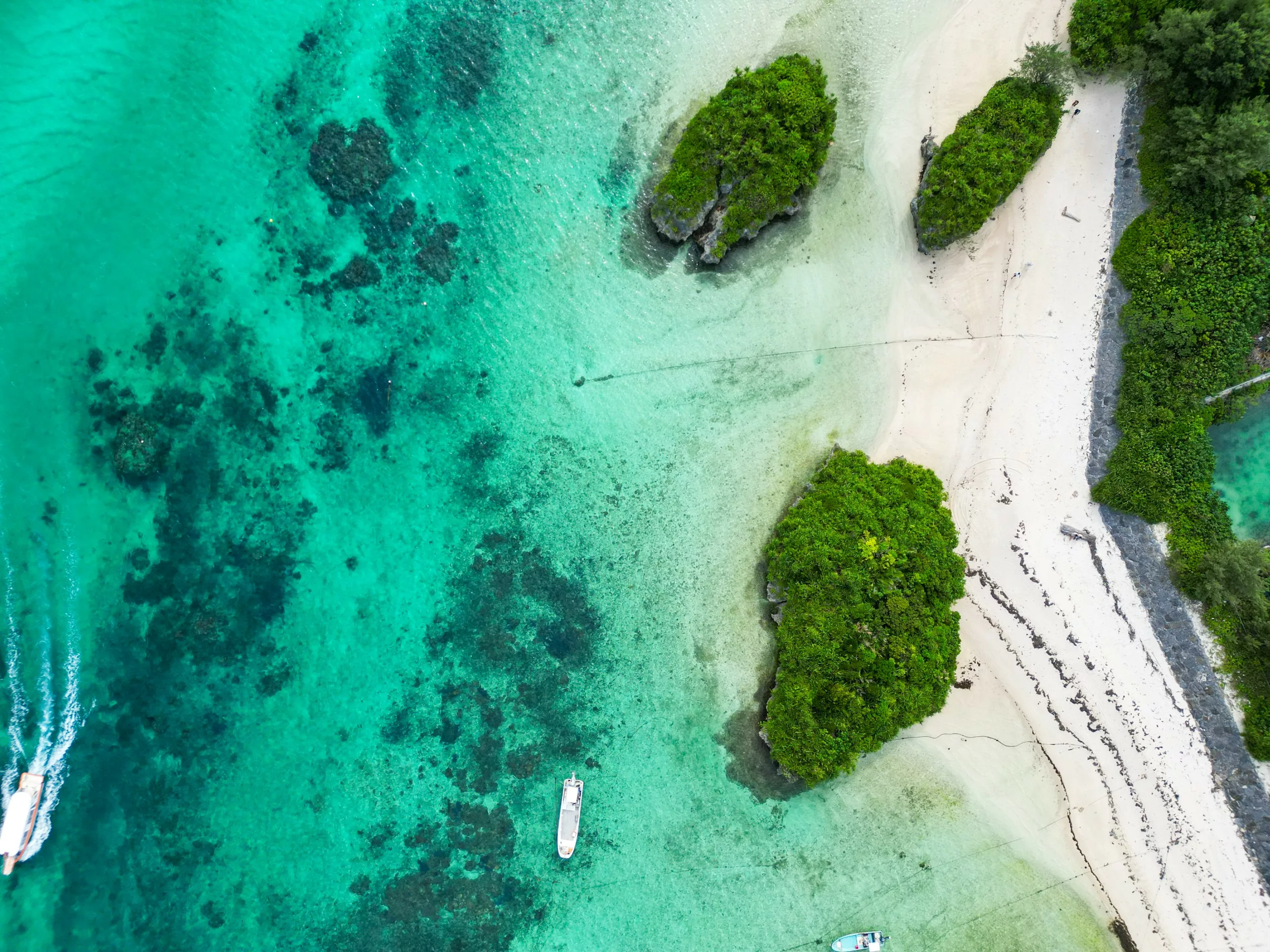 Vue aérienne d'une plage tropicale à Ishigaki, avec ses eaux turquoise cristallines, son sable blanc, ses îles verdoyantes, ses récifs coralliens visibles et ses bateaux