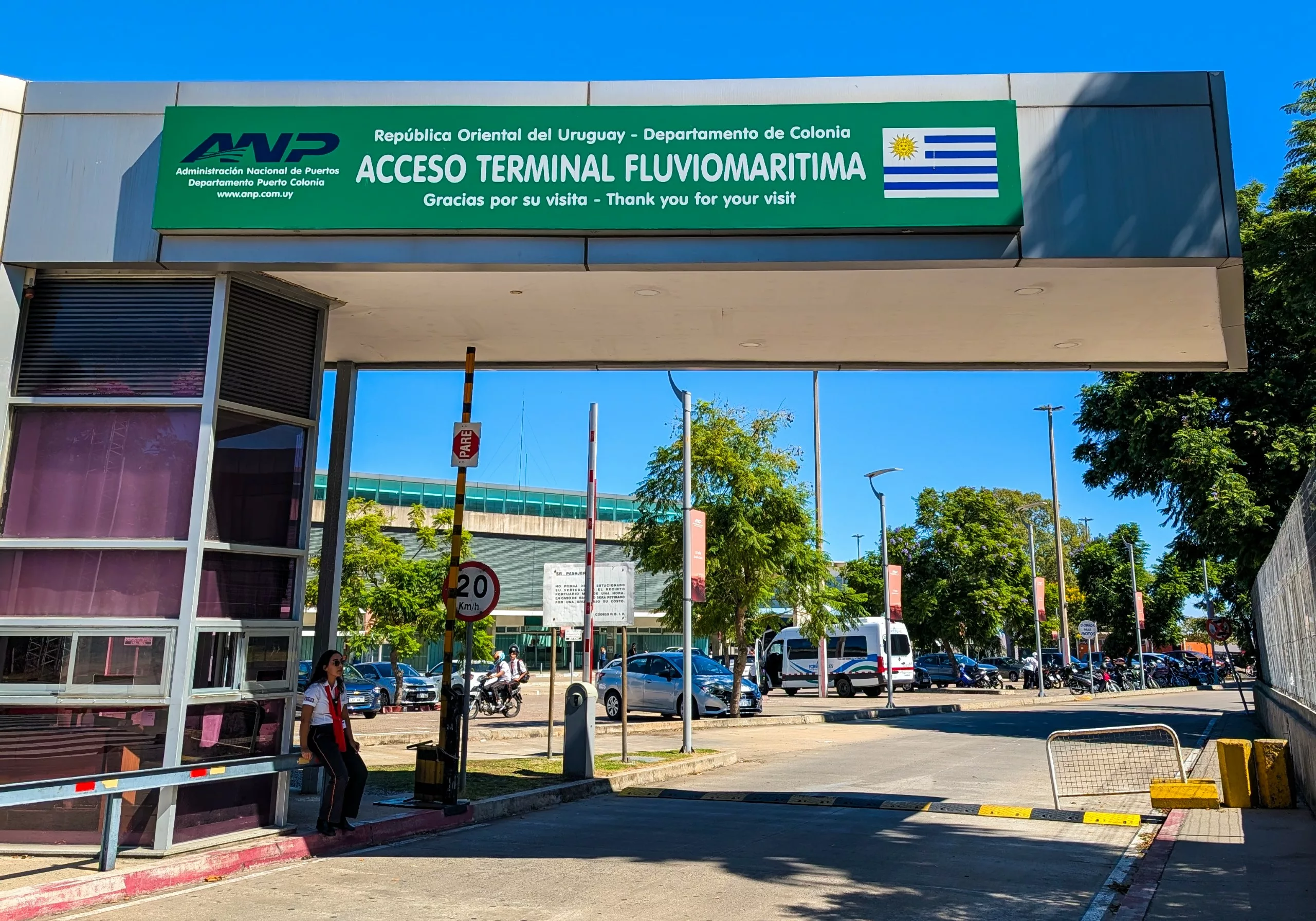 Entrée du terminal maritime de Colonia del Sacramento, en Uruguay, avec un panneau bilingue vert, des arbres, des voitures garées.