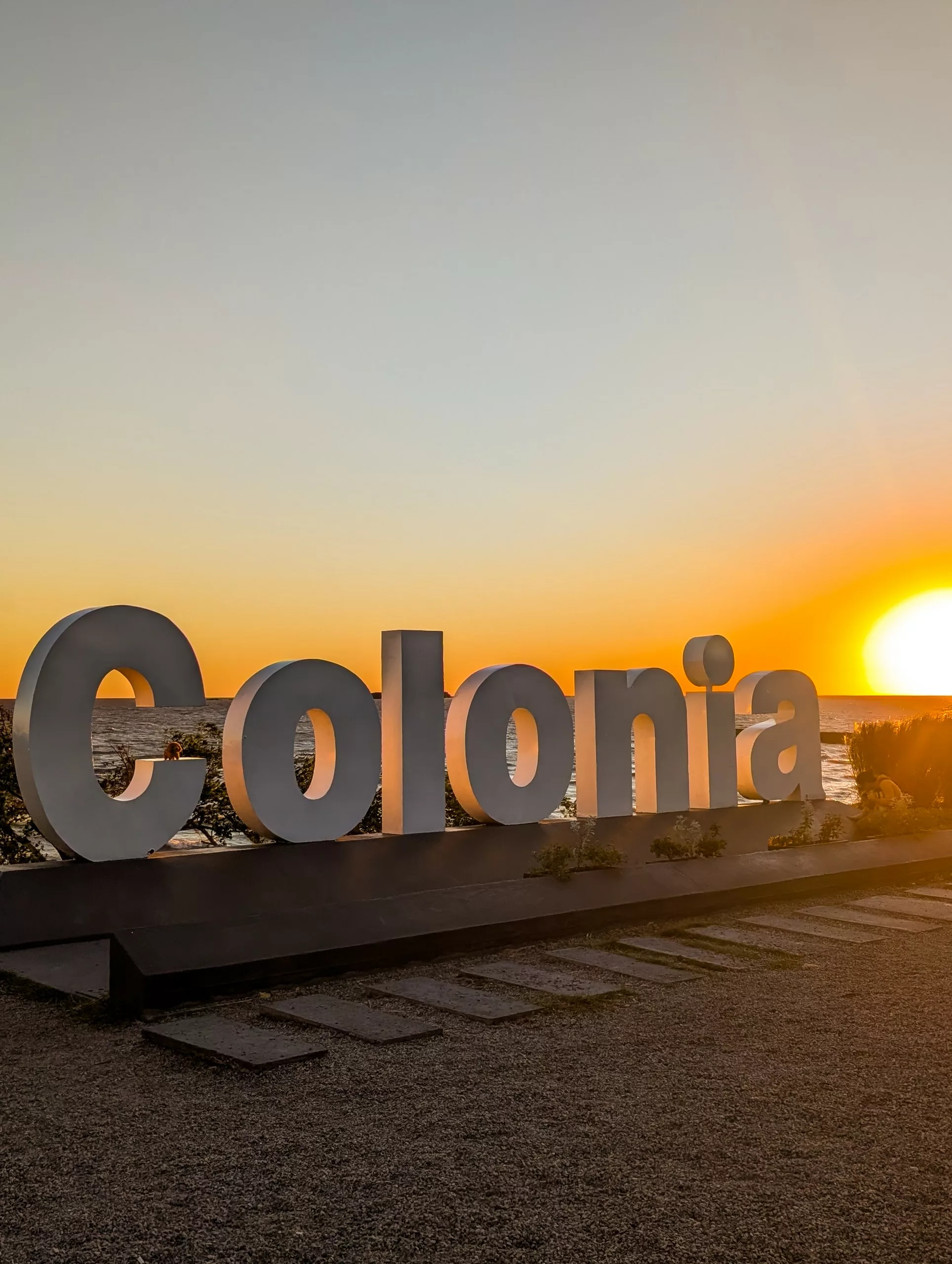 Lettres de Colonia devant l'océan, avec le soleil couchant sur la droite.