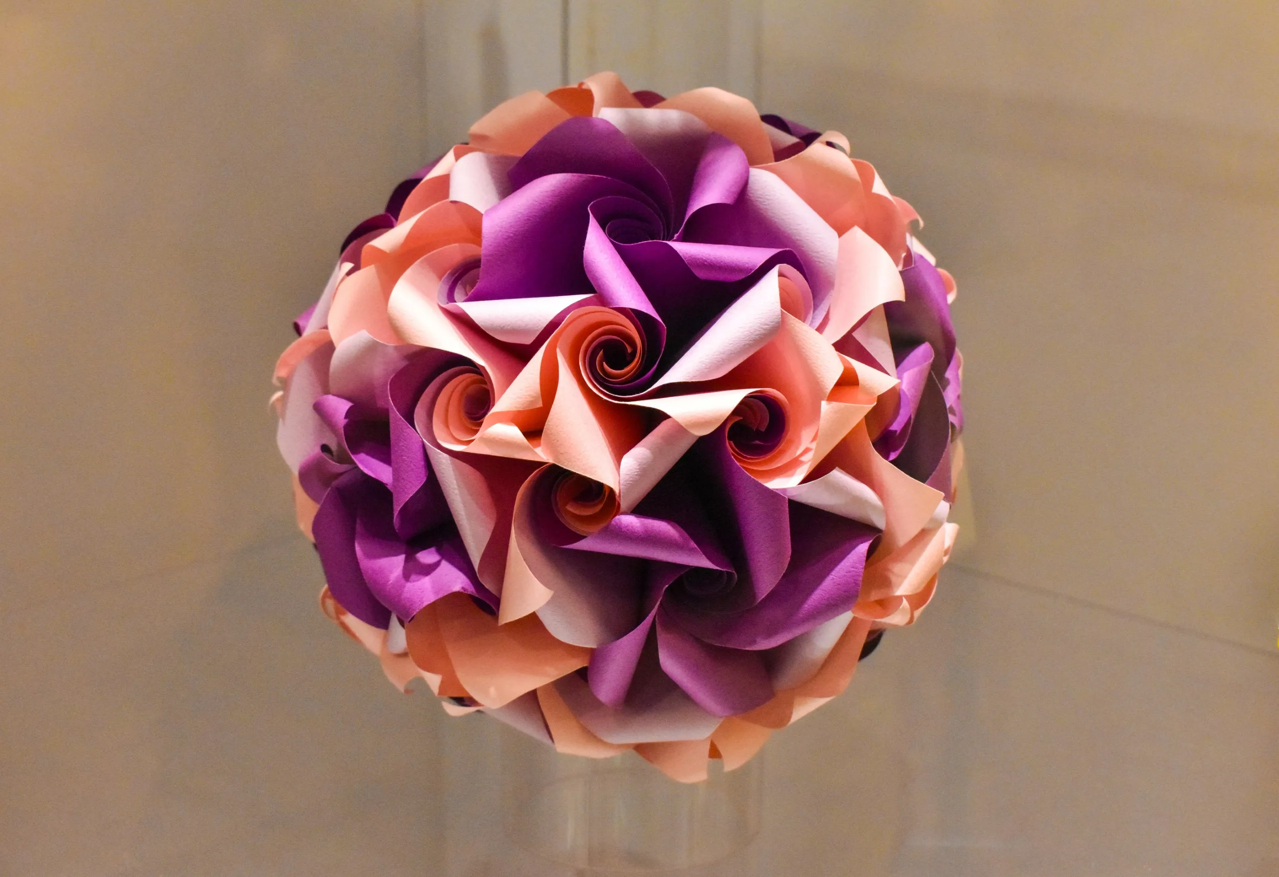 Un bouquet sphérique composé de papier plié avec minutie dans des tons de violet, de rose et de pêche, disposé à la manière d'une rose.