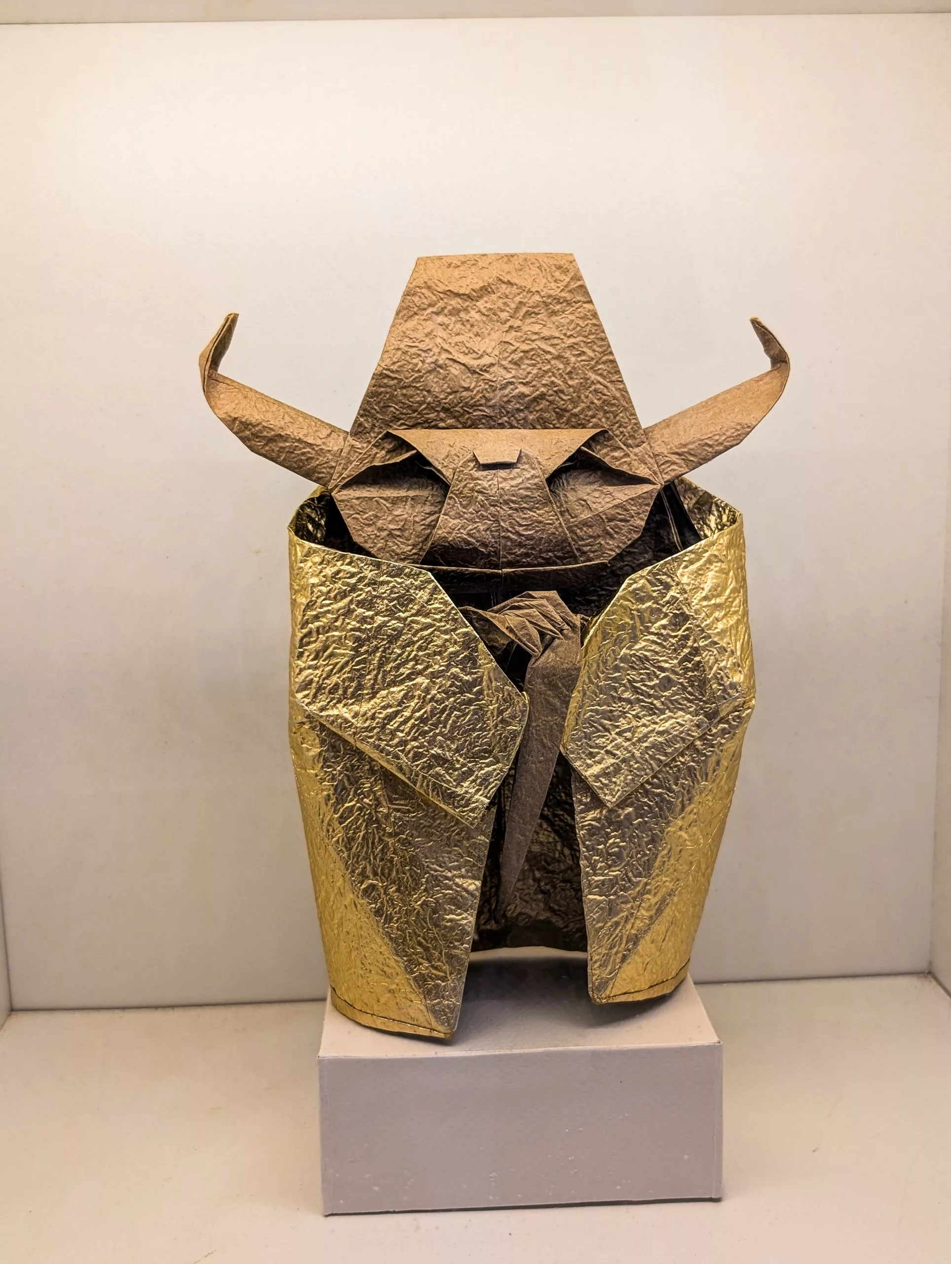Une figurine en origami texturée, vêtue d'une cape dorée et dotée d'une tête brune, représentant Yoda de Star Wars : un personnage aux oreilles pointues avec une robe.