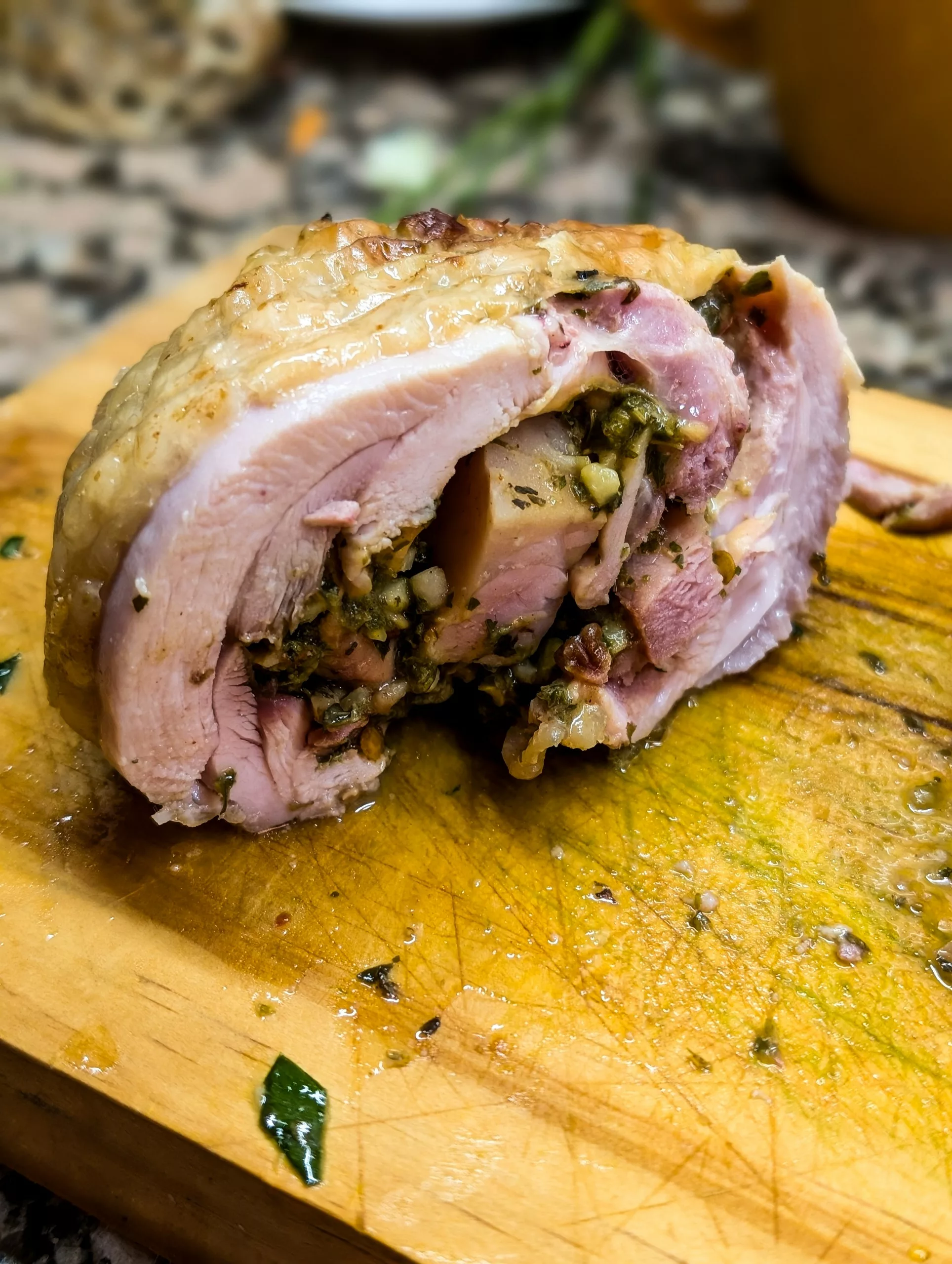 Une roulade tranchée, farcie d’herbes et de légumes, repose sur une planche à découper en bois ; son jus se mêle aux herbes fraîches