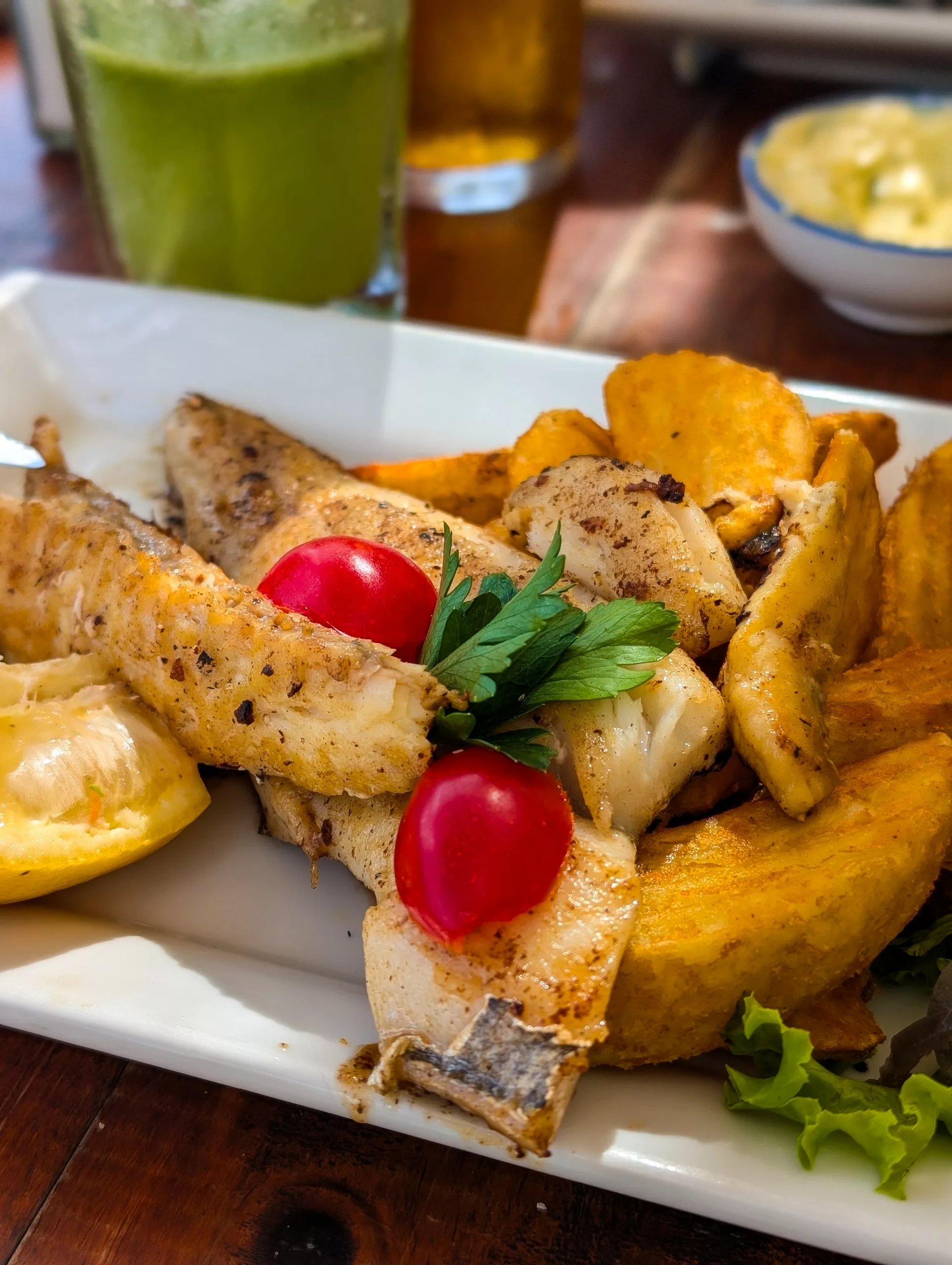 Un gros plan sur une assiette blanche avec du poisson, des grosses frites, quelques tomates cerises et des tranches de citron.