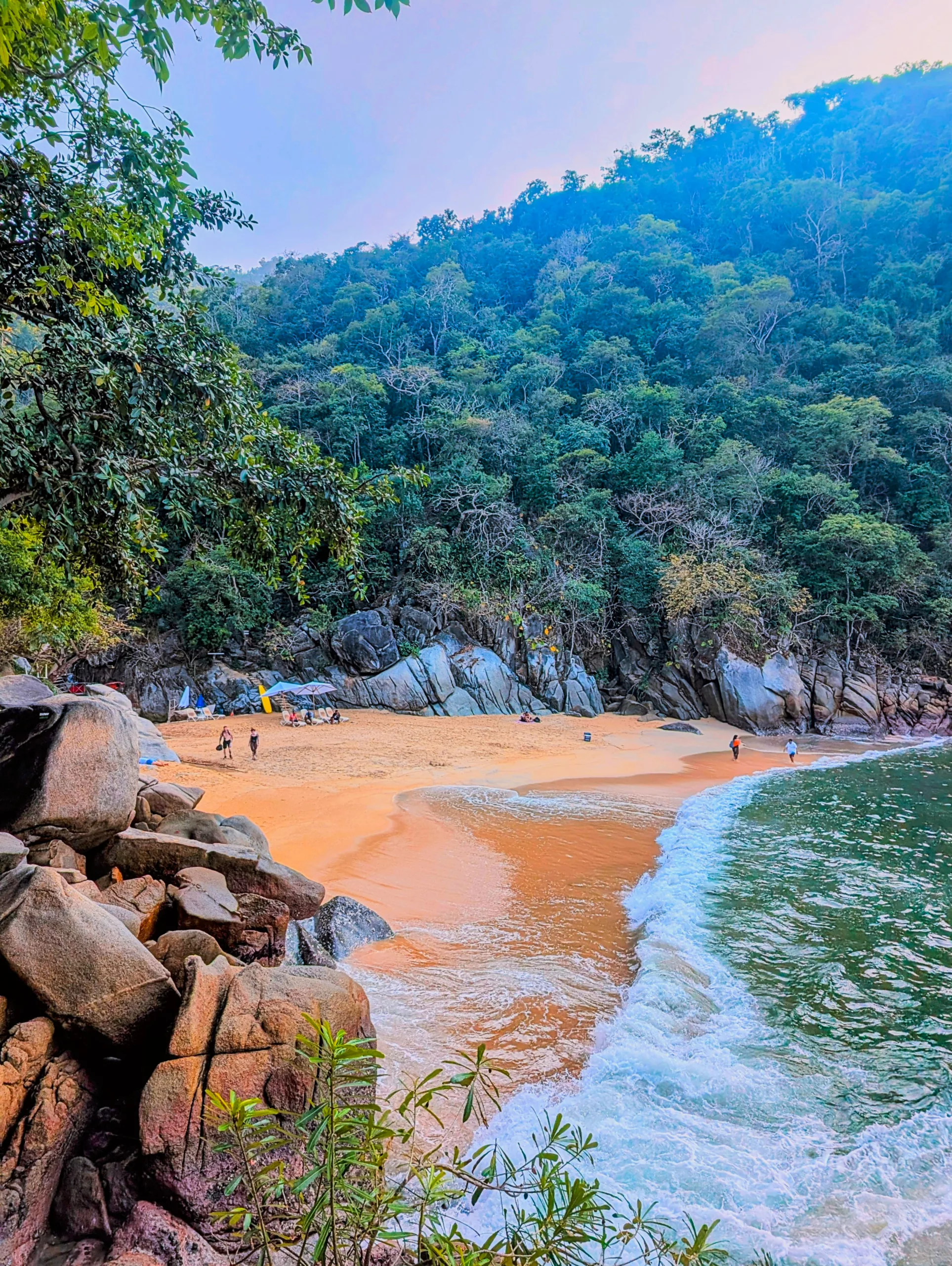 Une petite plage de sable bordée de rochers et d'une forêt verdoyante et dense.