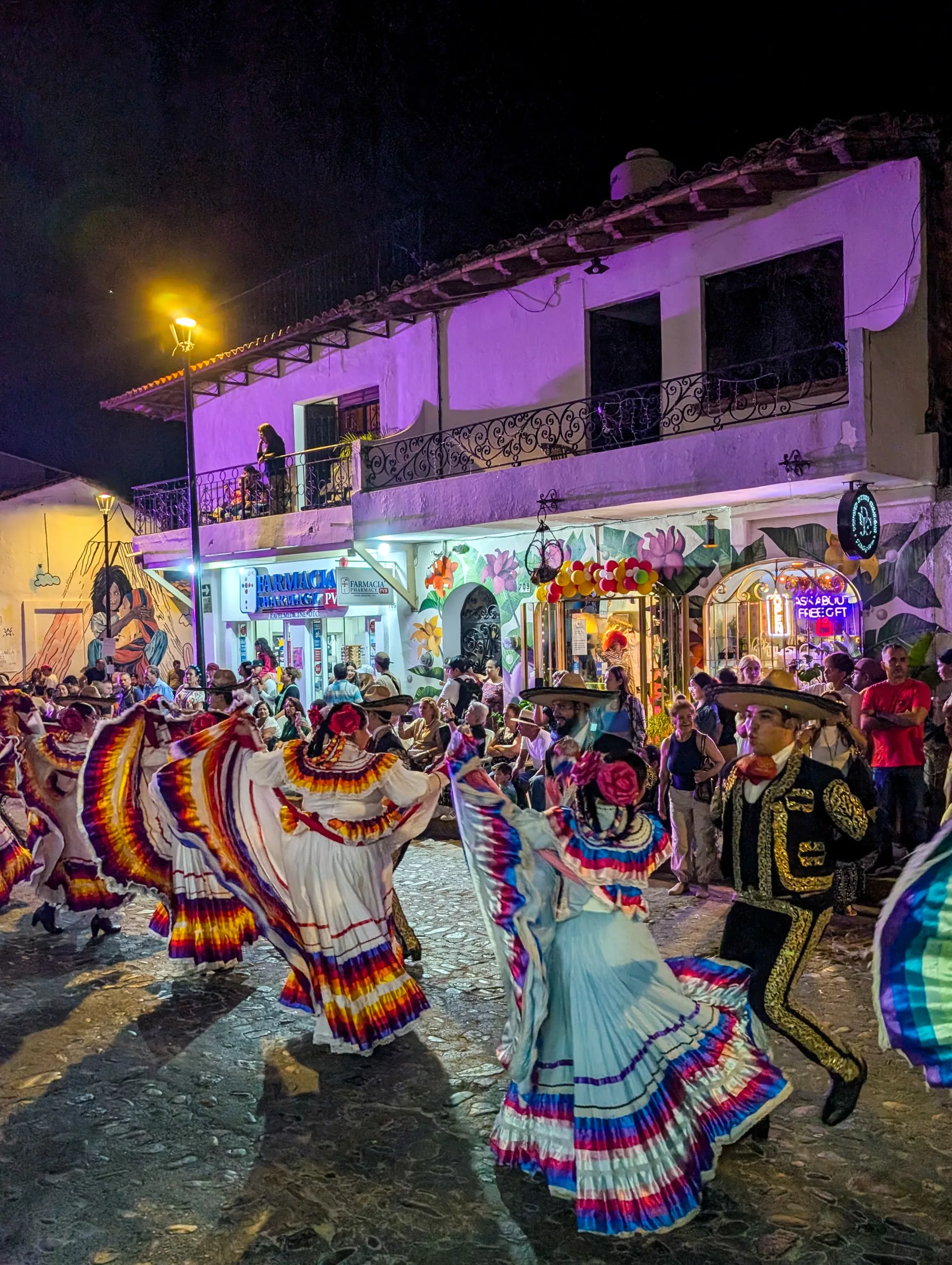 Des danseurs vêtus de costumes traditionnels mexicains se produisent dans la rue, la nuit, devant un bâtiment illuminé à Puerto Vallarta durant les fêtes de Guadalupe.